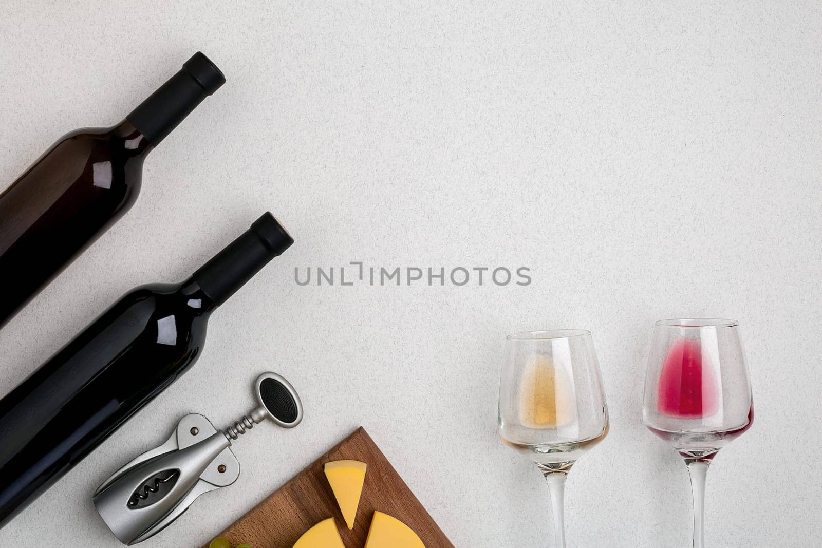 Two glasses of white and red wine and cheese. Two bottles of wine and a corkscrew. Top view with copy space