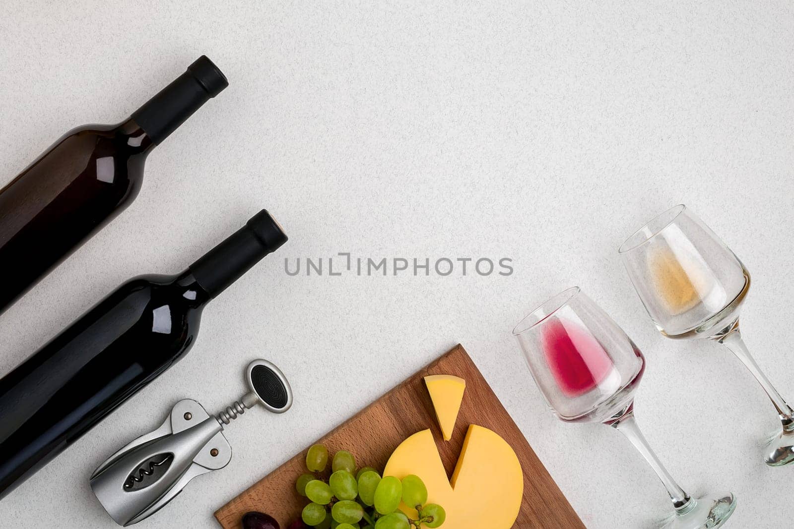 Two glasses of white and red wine, cheese and grapes. Two bottles of wine and a corkscrew. Top view with copy space