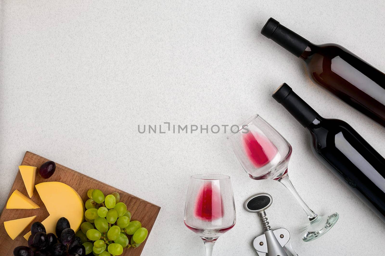 Two glasses of red wine, cheese and grapes. Two bottles of wine and a corkscrew. Top view with copy space