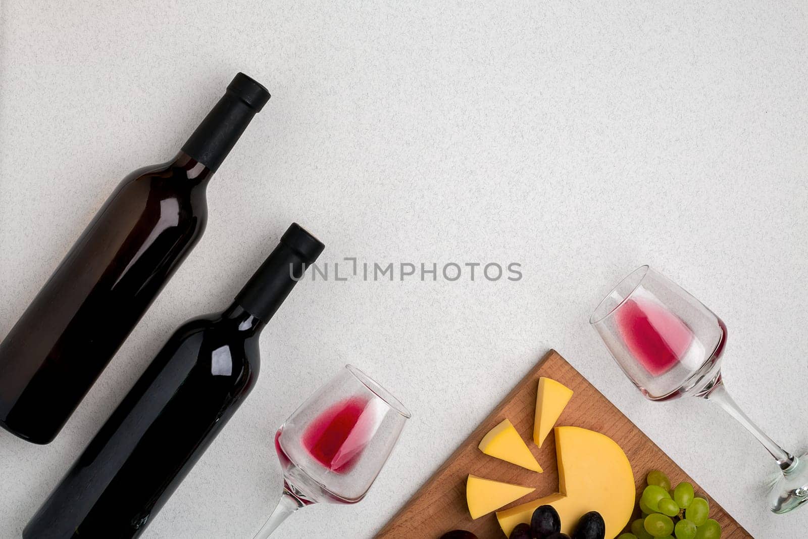 Two glasses of red wine, cheese and grapes. Two bottles of wine and a corkscrew. Top view with copy space