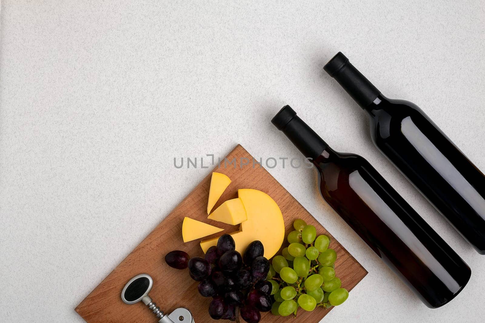 Two bottles of white and red wine, cheese and grapes. Top view with copy space