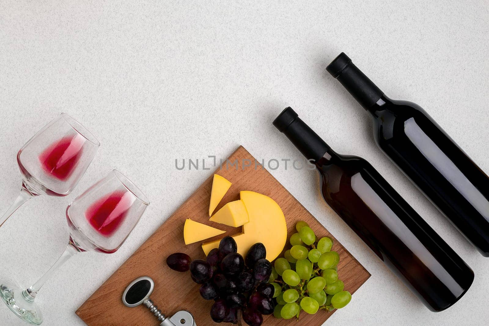 Two glasses of red wine, cheese and grapes. Two bottles of wine and a corkscrew. Top view with copy space