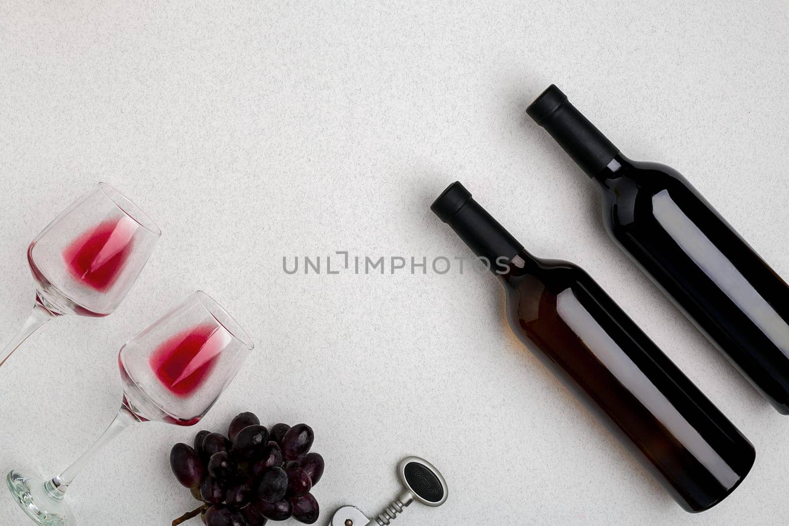 Two glasses of red wine and grapes. Two bottles of wine and a corkscrew. Top view with copy space