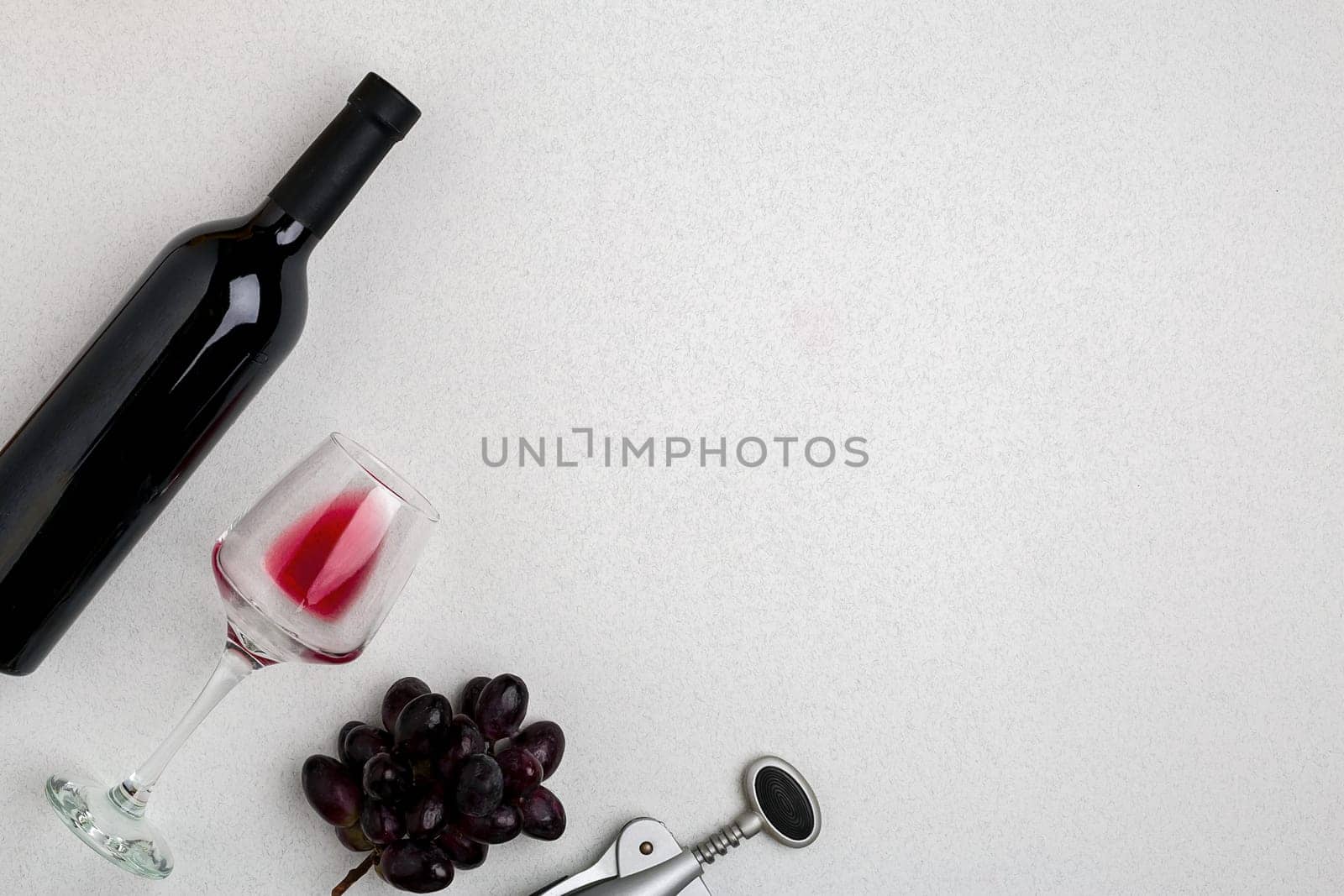 Overhead angled view of a large bottle of red wine, drinking glass on white background. Top view. Copy space