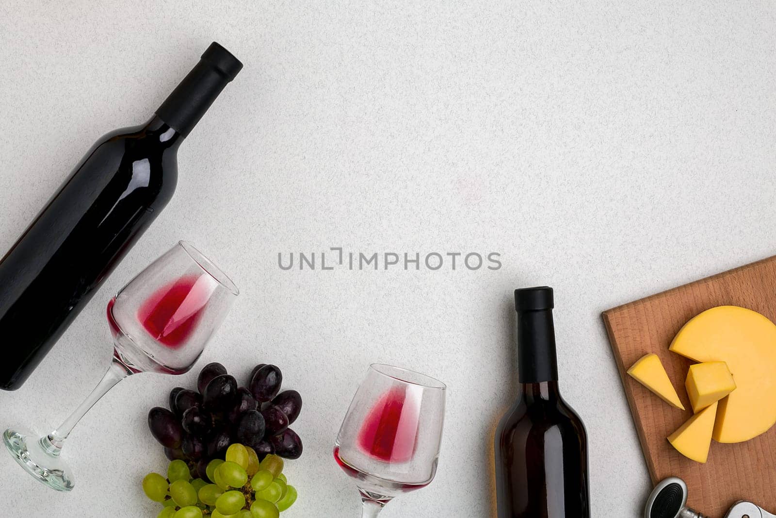 Two glasses of red wine, cheese and grapes. Two bottles of wine and a corkscrew. Top view with copy space