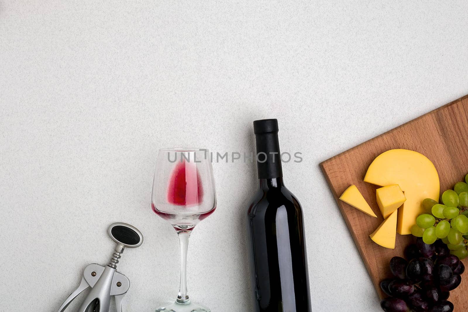 Glass of red wine, cheese and grapes. Bottle of wine and a corkscrew. Top view with copy space