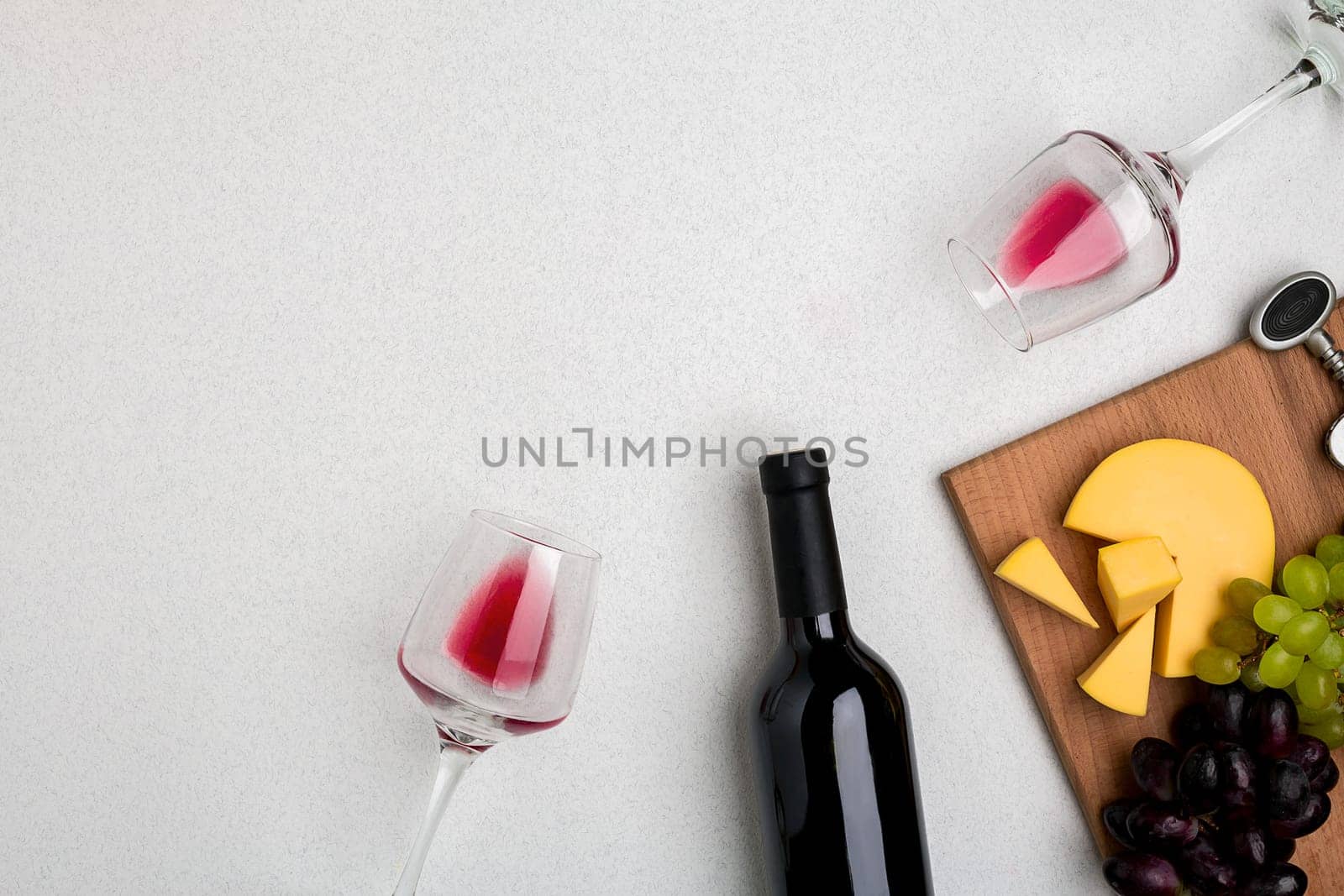 Two glasses of red wine, cheese and grapes. Bottle of wine and a corkscrew. Top view with copy space