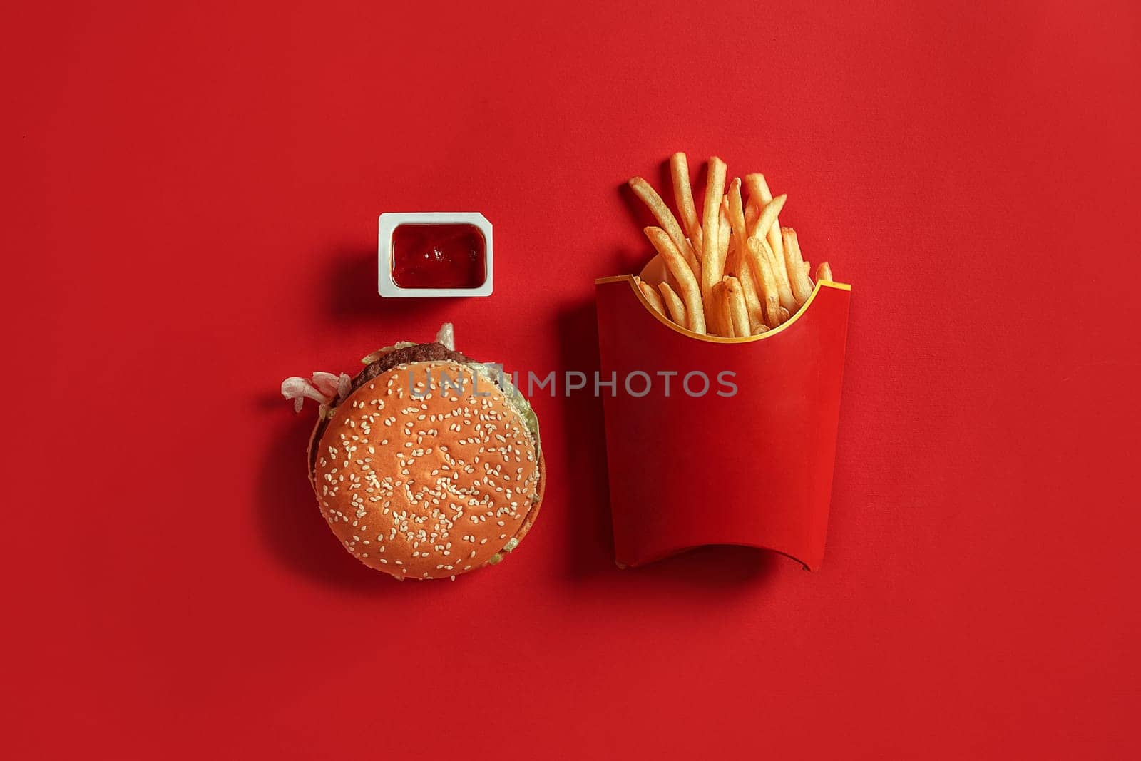 Burger and Chips. Hamburger and french fries in red paper box. Fast food on red background. Hamburger with tomato sauce. Top view, flat lay with copyspace