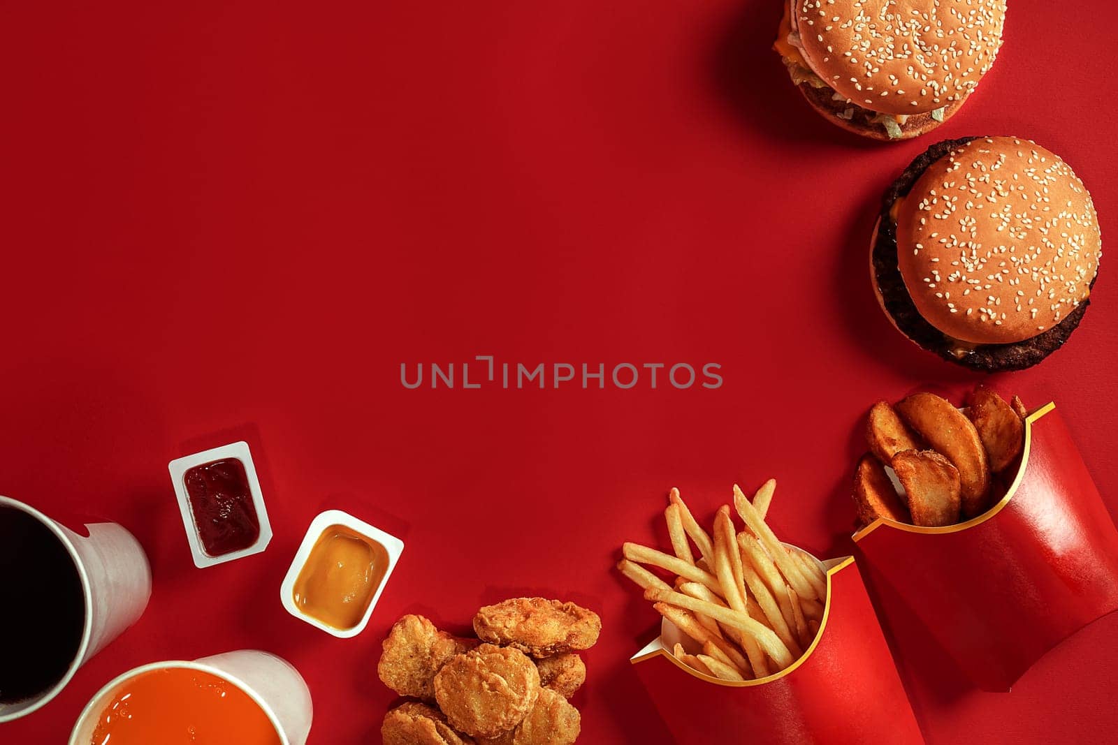 Two hamburgers and french fries, sauces and drinks on red background. Fast food. Hamburger with chicken nuggets. Top view, flat lay with copyspace.