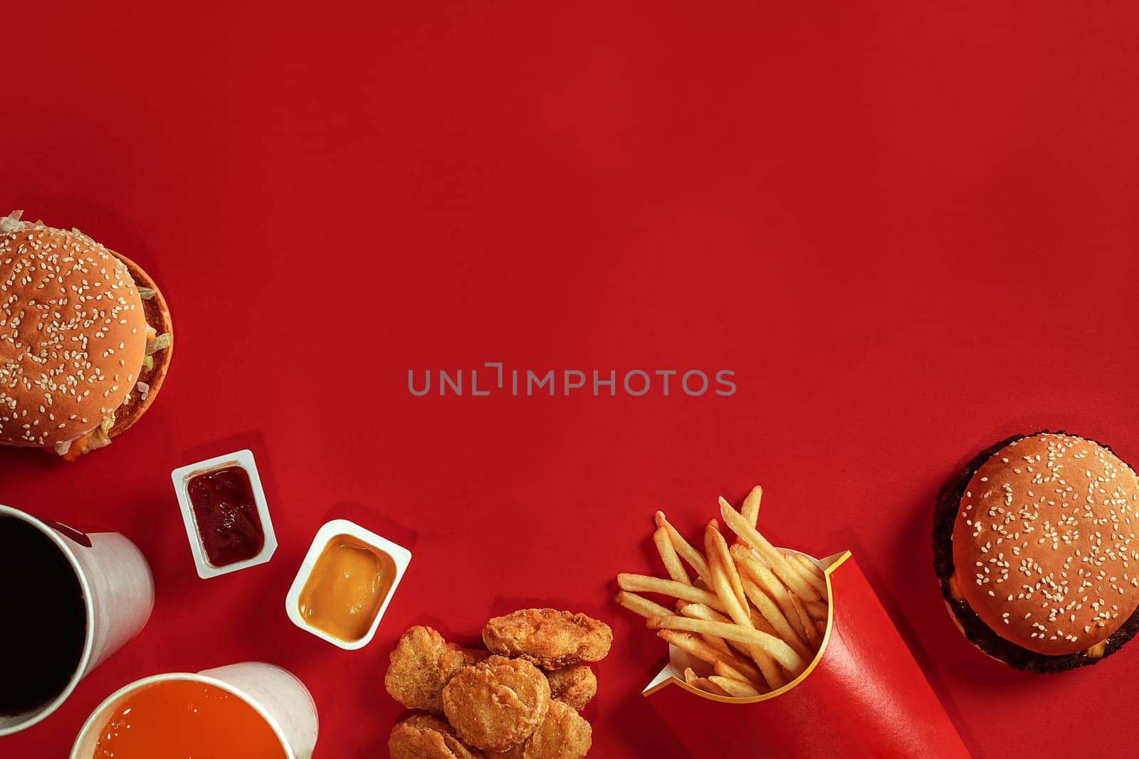 Two hamburgers and french fries, sauces and drinks on red background. Fast food. Hamburger with chicken nuggets. Top view, flat lay with copyspace.