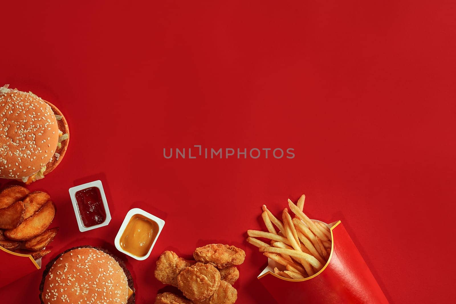 Burger and Chips. Hamburger and french fries in red paper box. Fast food on red background. Hamburger with tomato sauce. Top view, flat lay with copyspace
