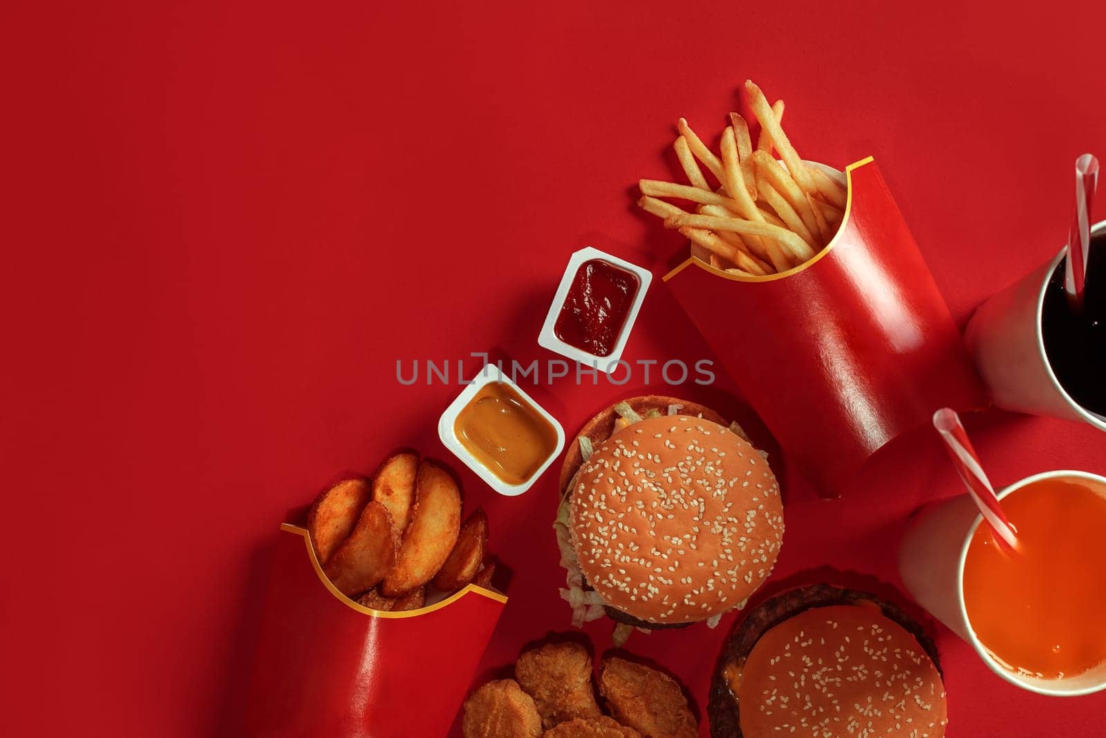 Two hamburgers and french fries, sauces and drinks on red background. Fast food. Hamburger with chicken nuggets. Top view, flat lay with copyspace.