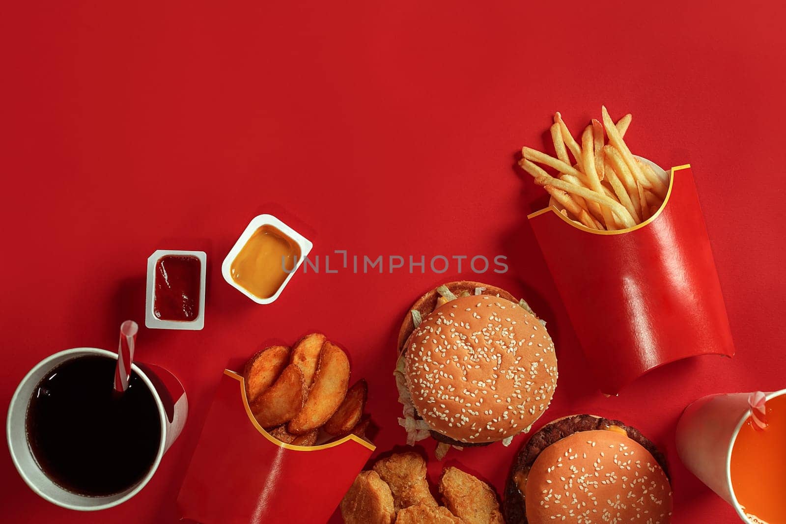 Two hamburgers and french fries, sauces and drinks on red background. Fast food. Hamburger with chicken nuggets. Top view, flat lay with copyspace.