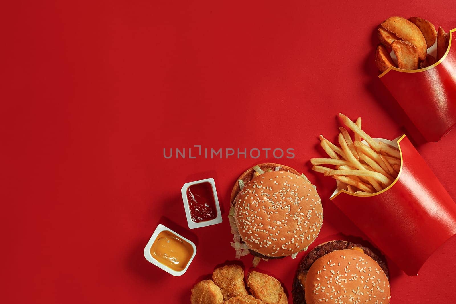 Two hamburgers and french fries, sauces on red background. Fast food. Top view, flat lay with copyspace.