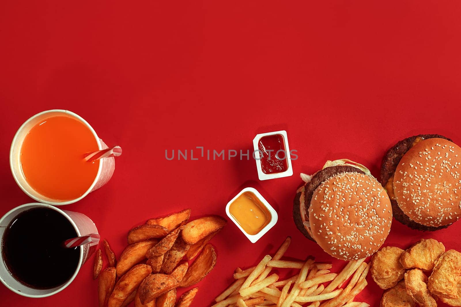 Burger and Chips. Hamburger and french fries in red paper box. Fast food on red background. Hamburger with tomato sauce. Top view, flat lay with copyspace