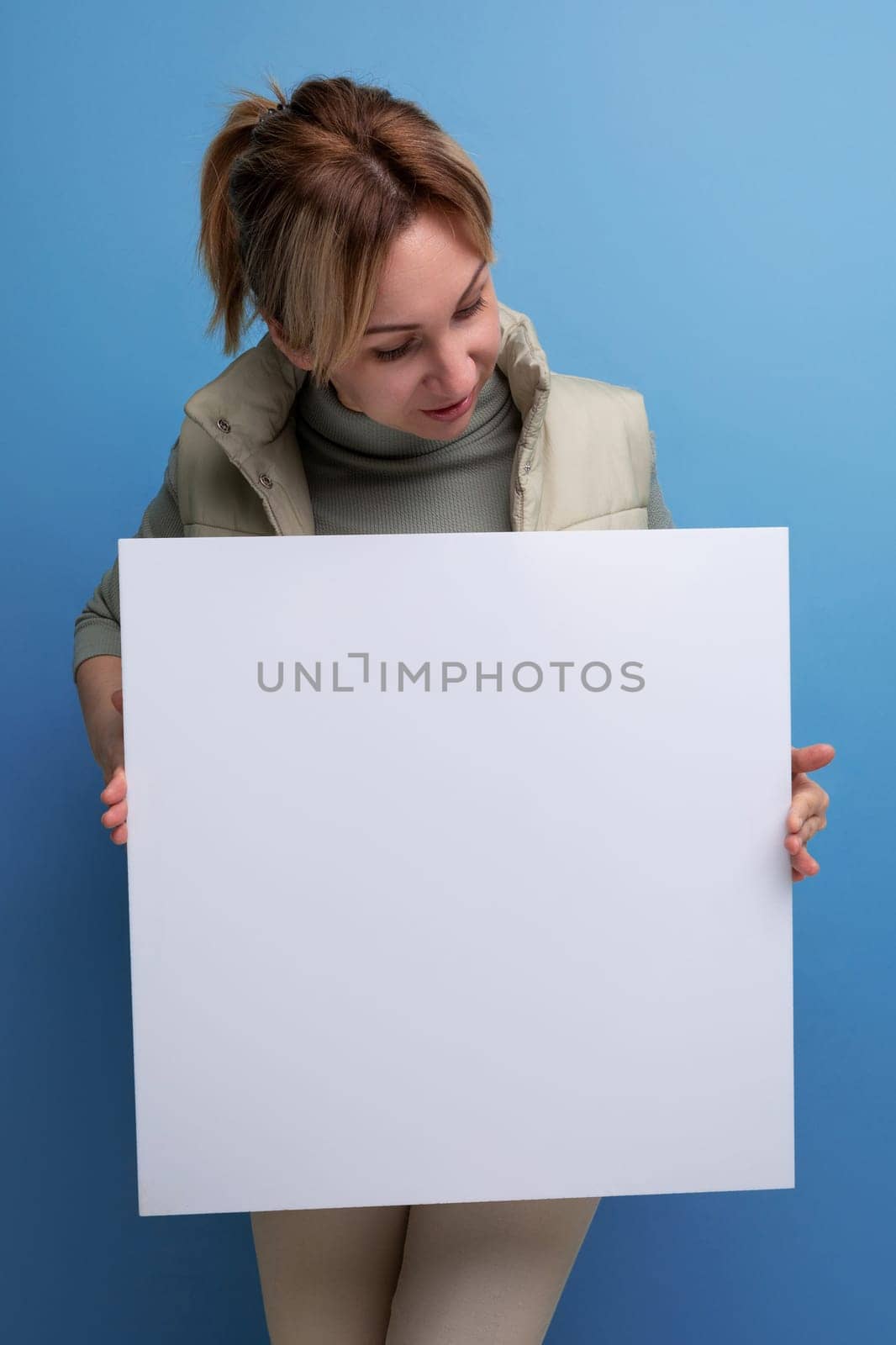 young blond hair woman holding a poster with a mockup for advertising.