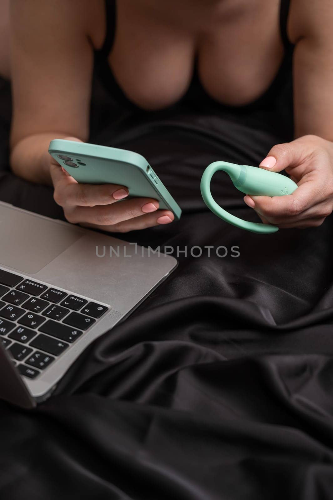 A woman lies on a bed and synchronizes the kegel machine with a smartphone. Girl watching video on laptop. by mrwed54