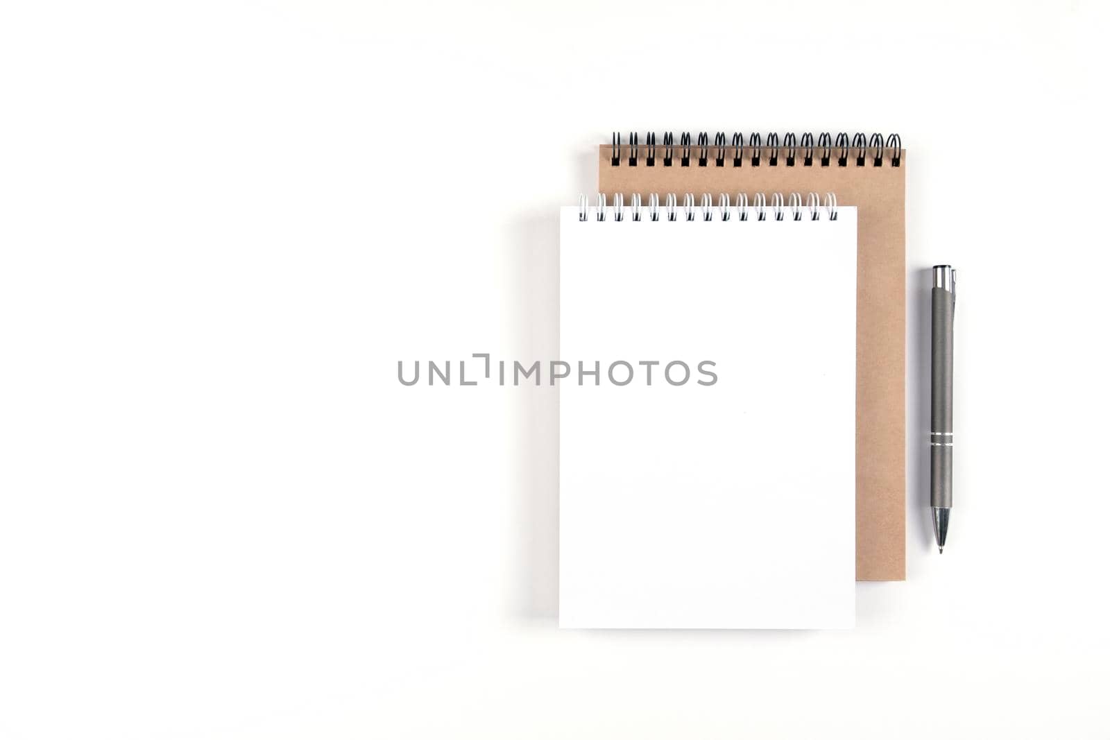 Two blank spiral notepads stacked on a white background next to an automatic pen. Notebooks with white and recycled sheets. Education, office.
