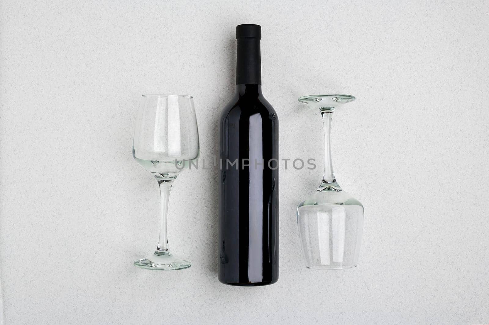 Overhead angled view of a large bottle of red wine, drinking glasses on white background. Top view. Copy space
