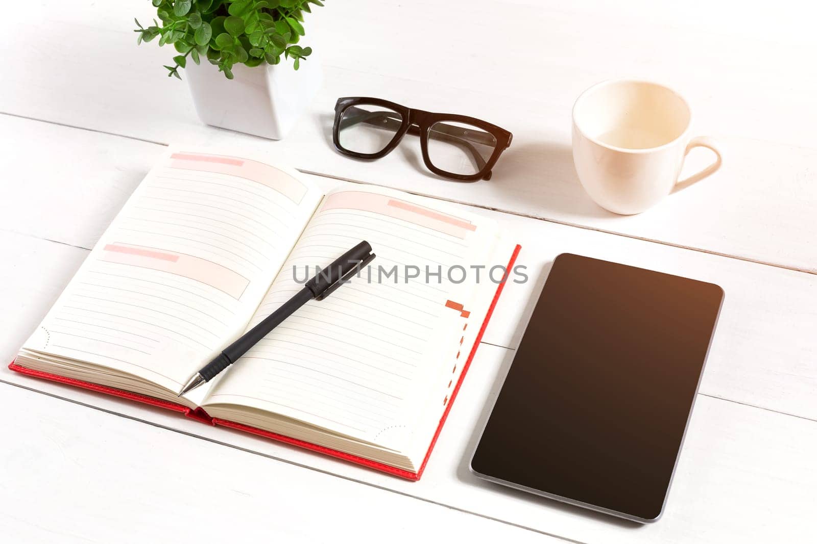 Stylish minimalistic workplace with tablet and notebook and glasses in flat lay style. White background. Top view. Copy space. sun flare