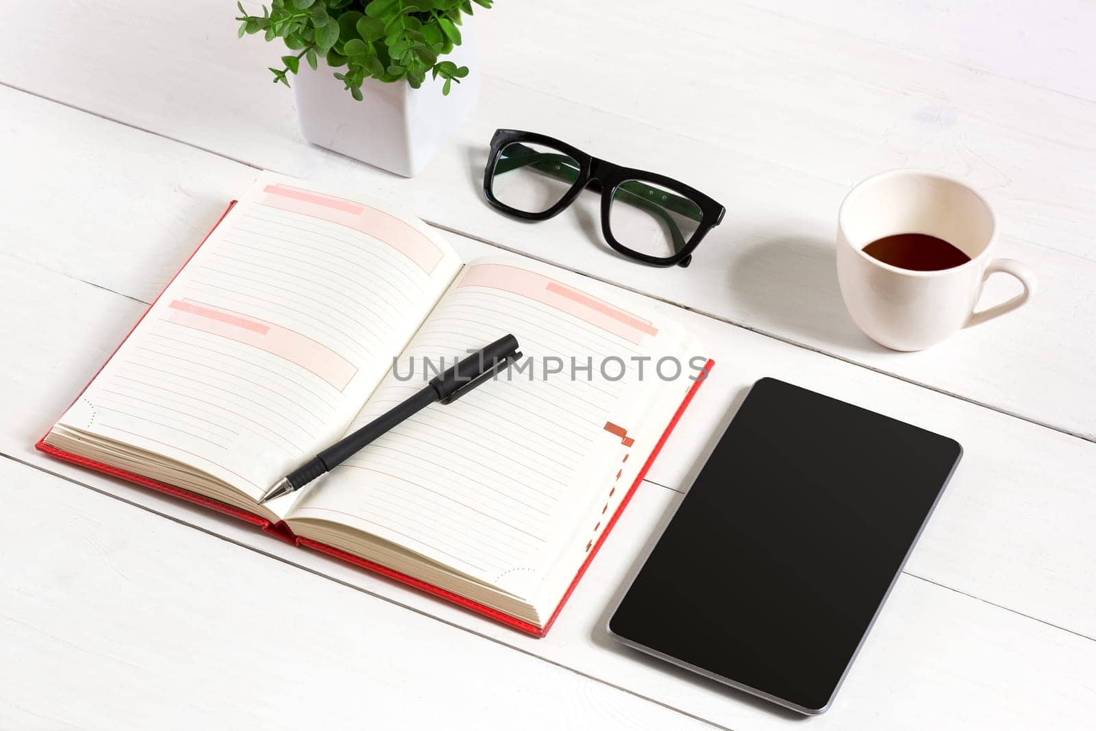 Office table desk with set of supplies, white blank notepad, cup, pen, tablet, glasses, flower on white background. Top view by nazarovsergey