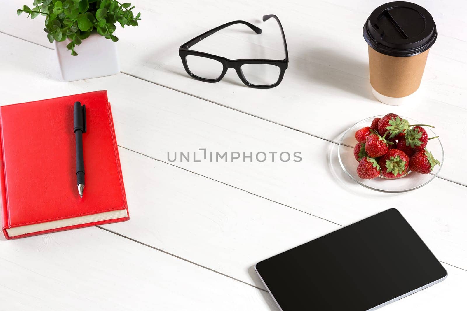 Office table desk with set of supplies, red notepad, cup, pen, tablet, glasses, flower on white background. Top view and copy space for text