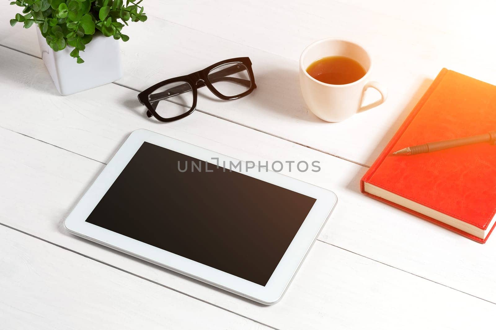 Office table desk with set of supplies, red notepad, cup, pen, tablet, glasses, flower on white background. Top view and copy space for text. sun flare