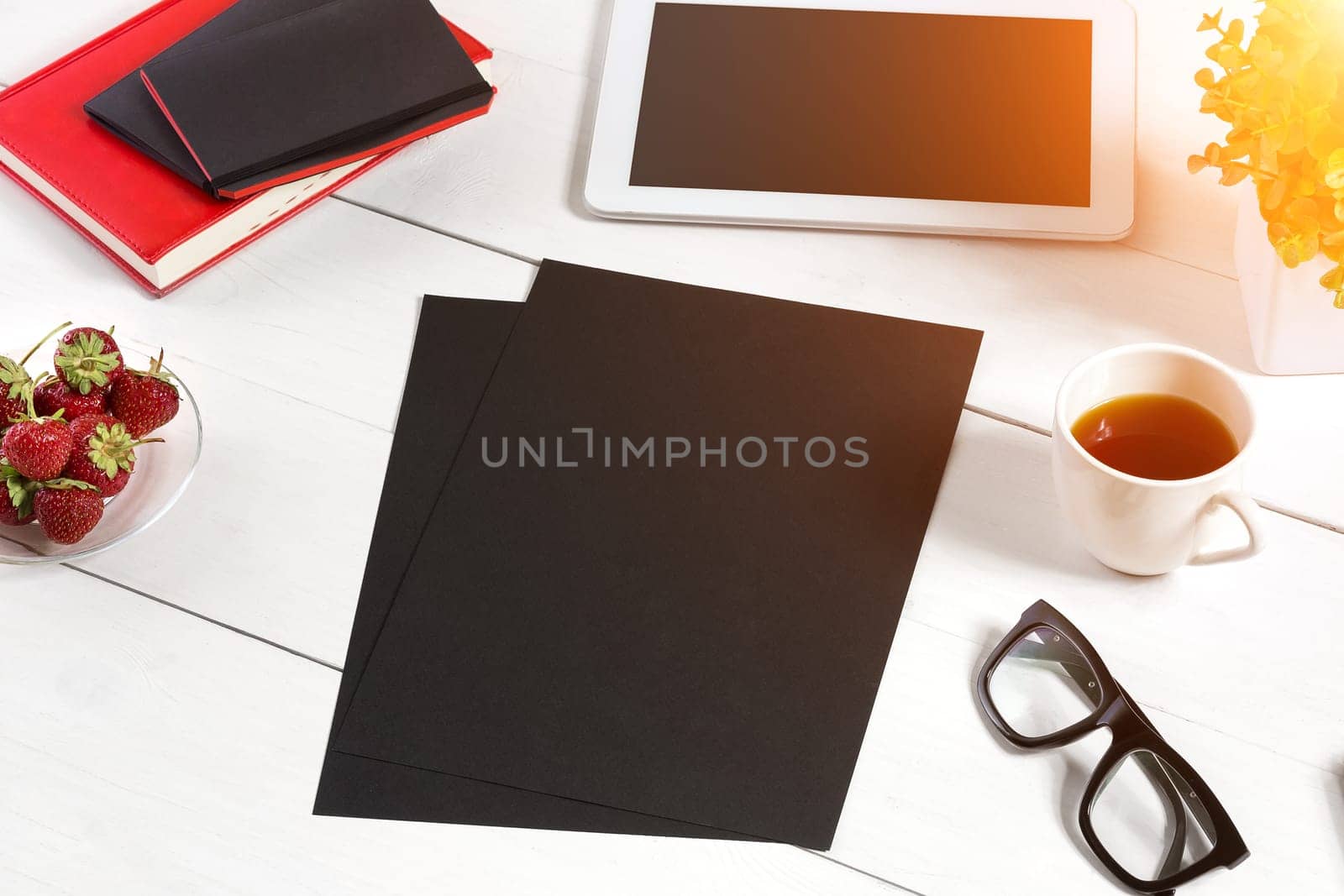 Stylish minimalistic workplace with tablet and notebook and glasses in flat lay style. White background. Top view. Copy space. sun flare