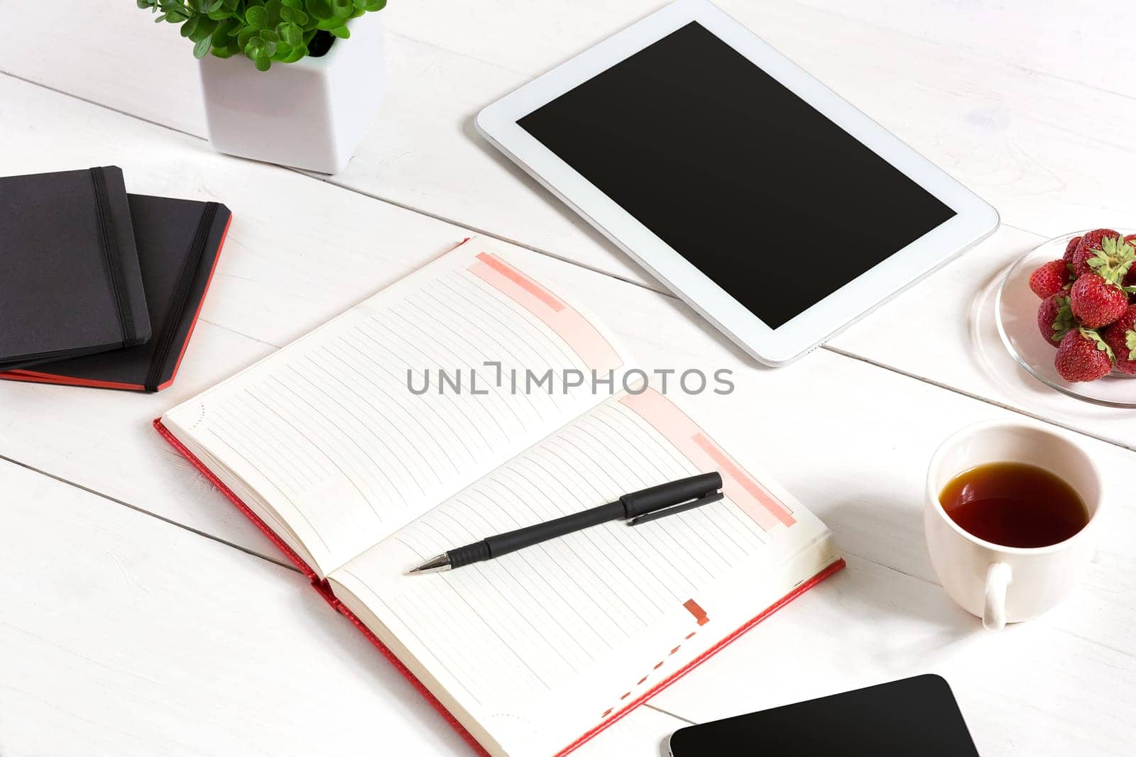 Office table desk with set of supplies, white blank notepad, cup, pen, tablet, flower on white background. Top view and copy space for text