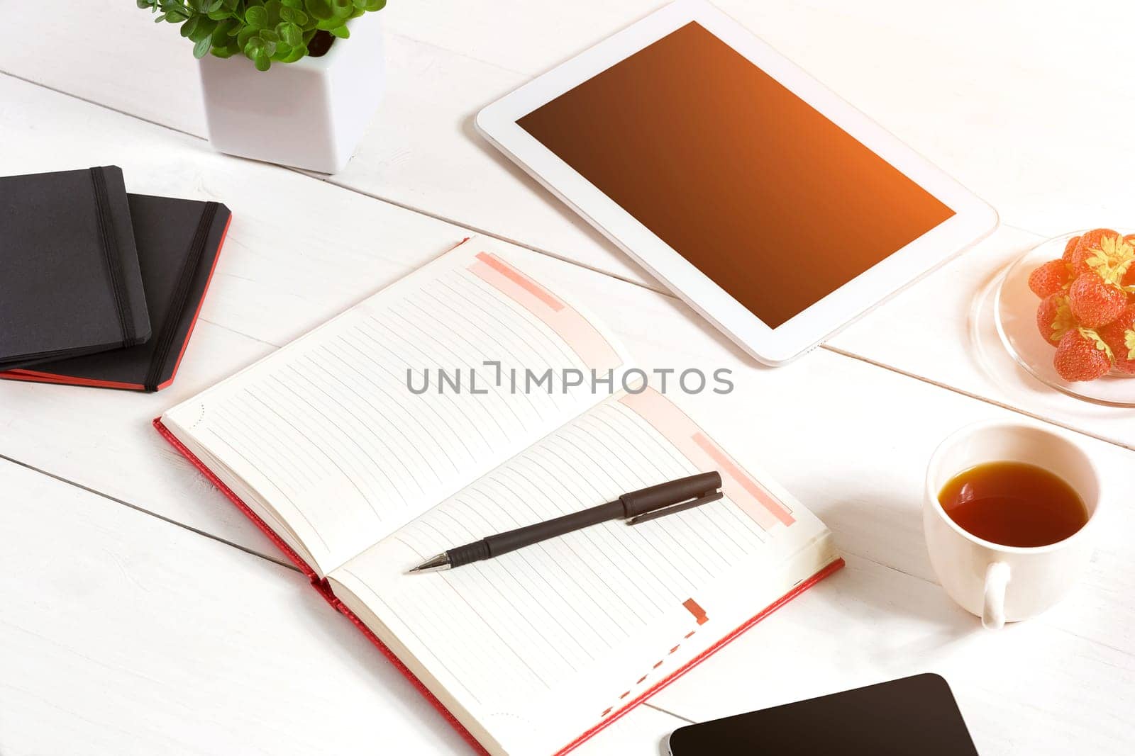 Office table desk with set of supplies, white blank notepad, cup, pen, tablet, flower on white background. Top view and copy space for text. sun flare