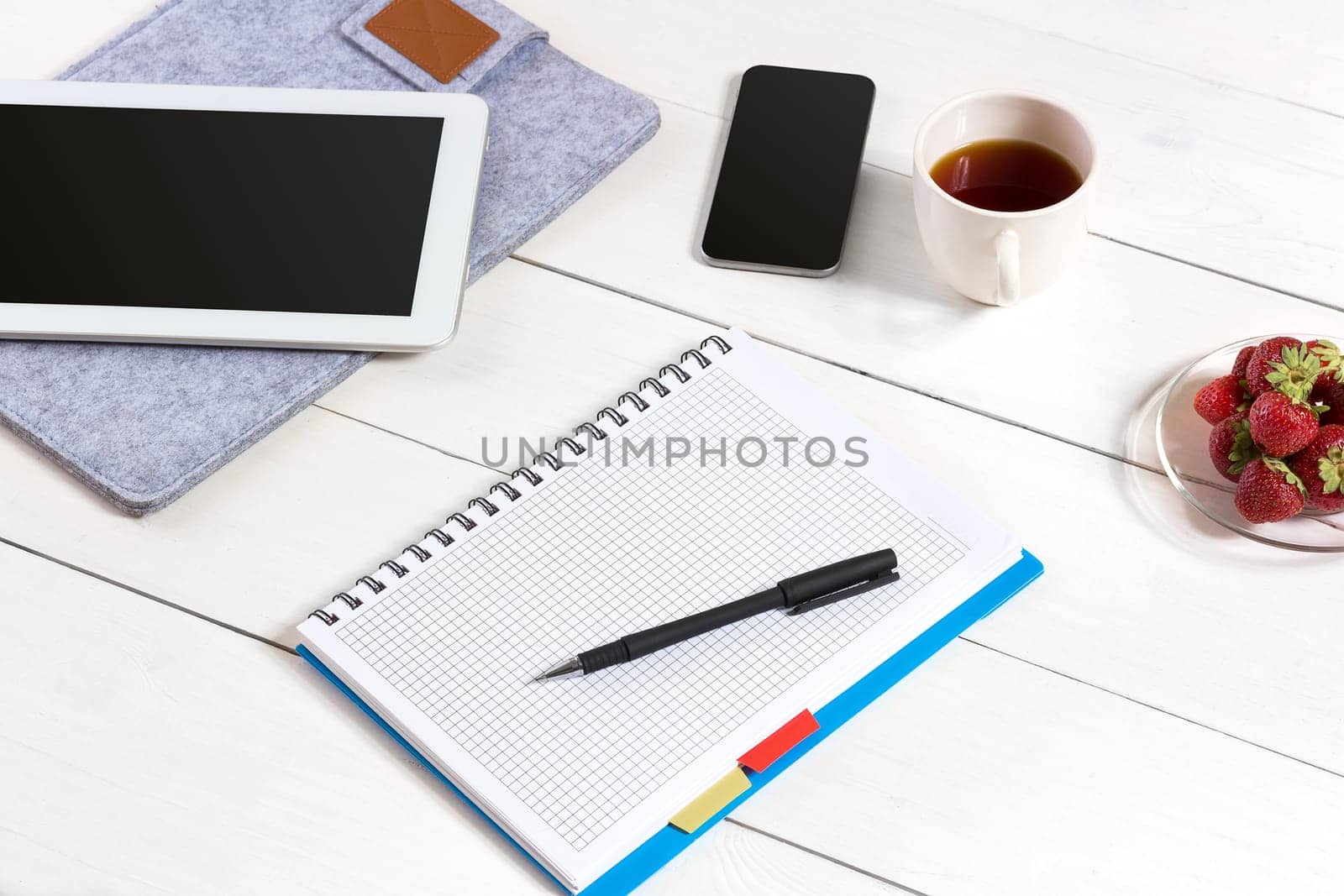 Office table desk with set of supplies, white blank notepad, cup, pen, tablet on white background. Top view and copy space for text