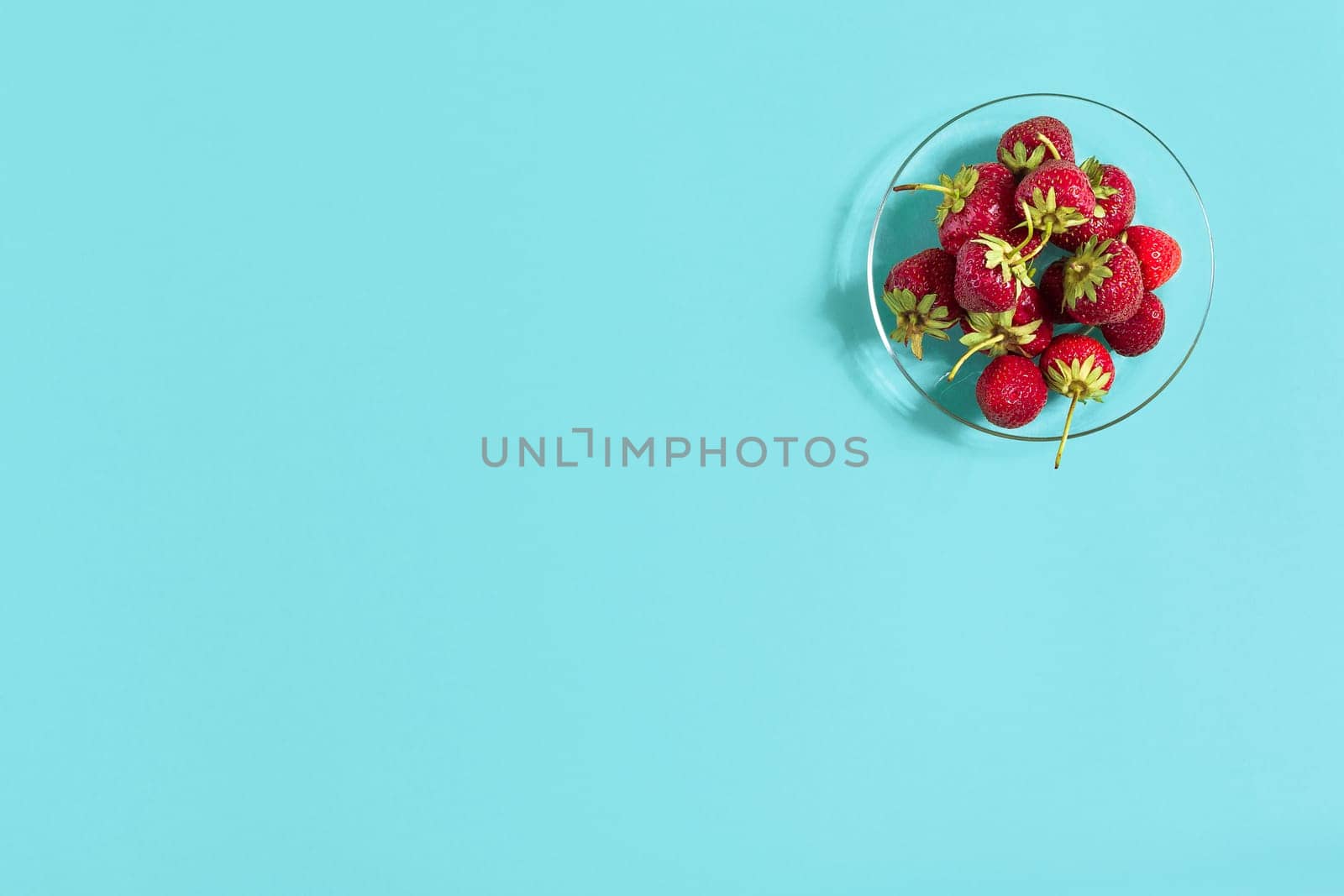 Ripe strawberries on the saucer isolated on mint background. Top view. Copy space. Still life mockup flat lay