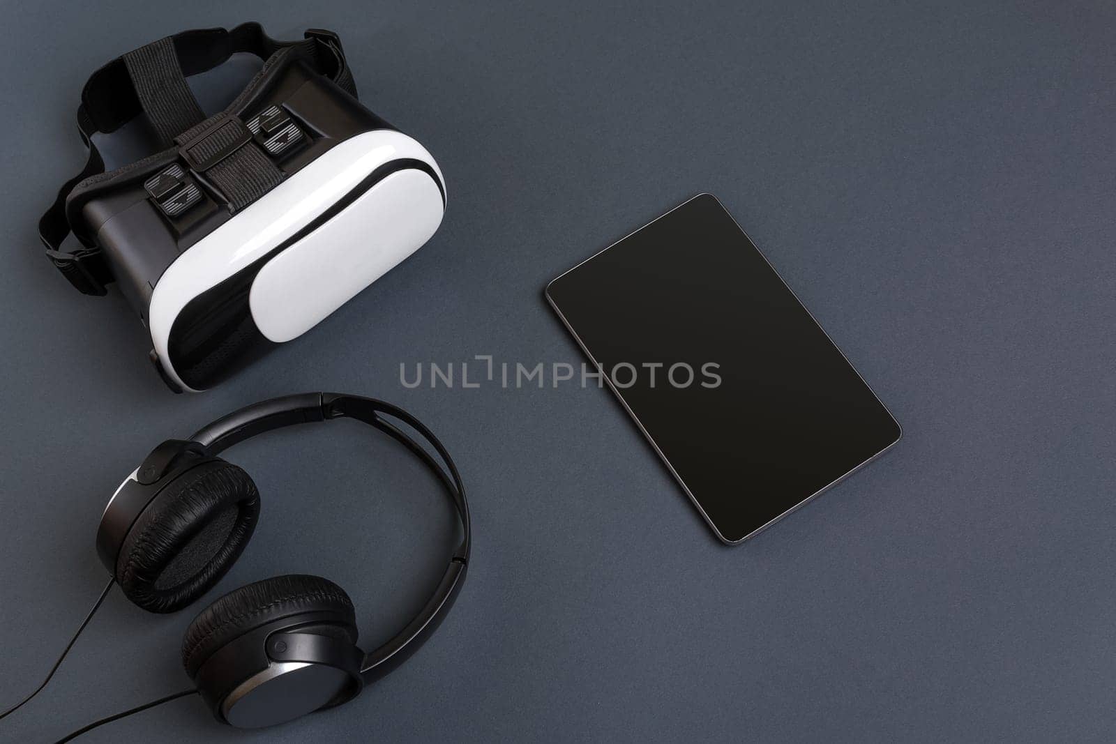 Virtual reality glasses and tablet with headphones on a gray background. Top view. Copy space