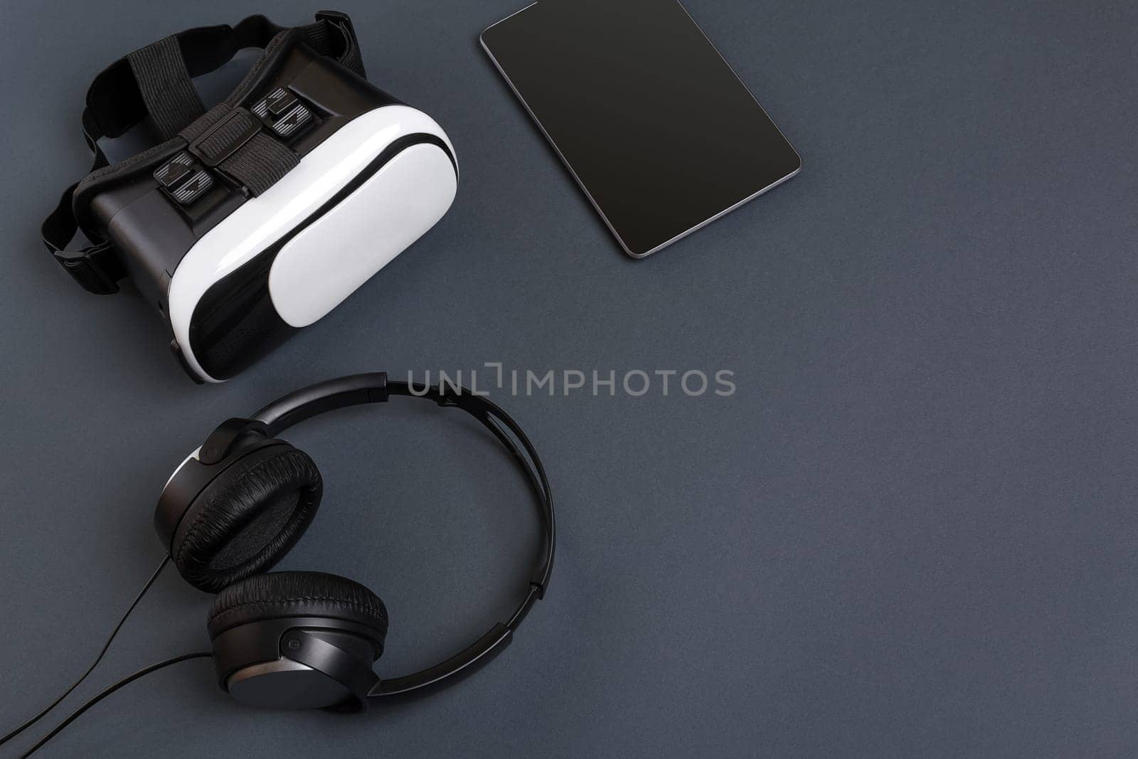 Virtual reality glasses and tablet with headphones on a gray background. Top view. Copy space