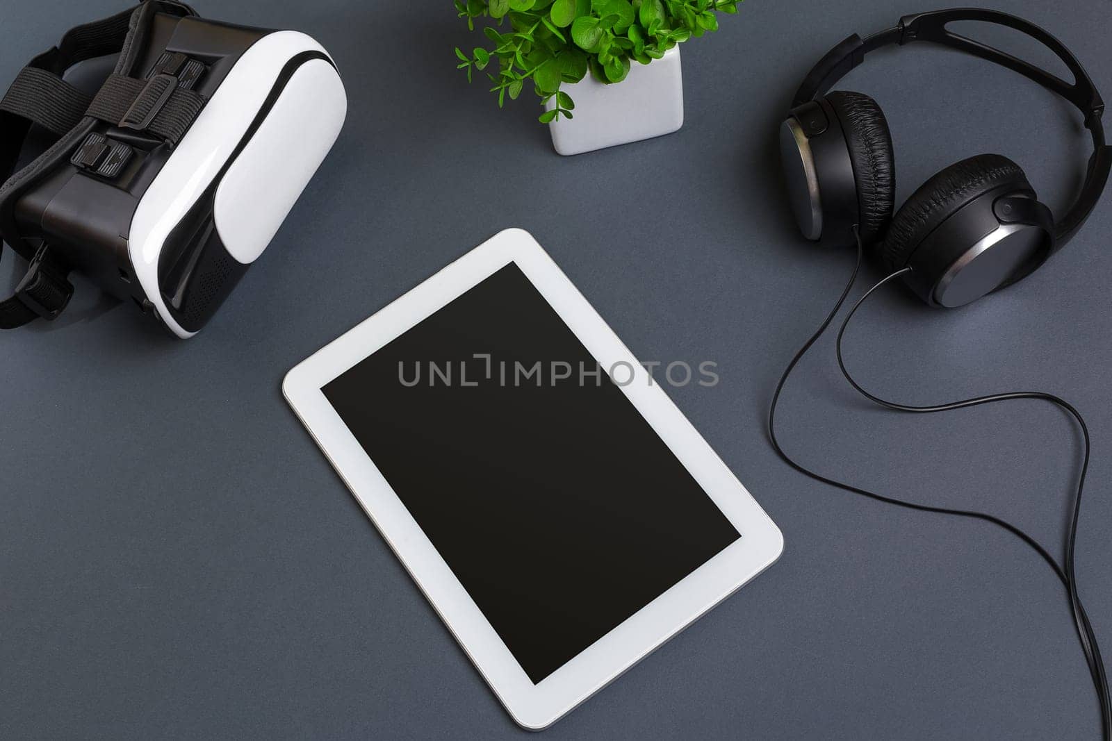 Virtual reality glasses and tablet with headphones on a gray background. Top view. Copy space