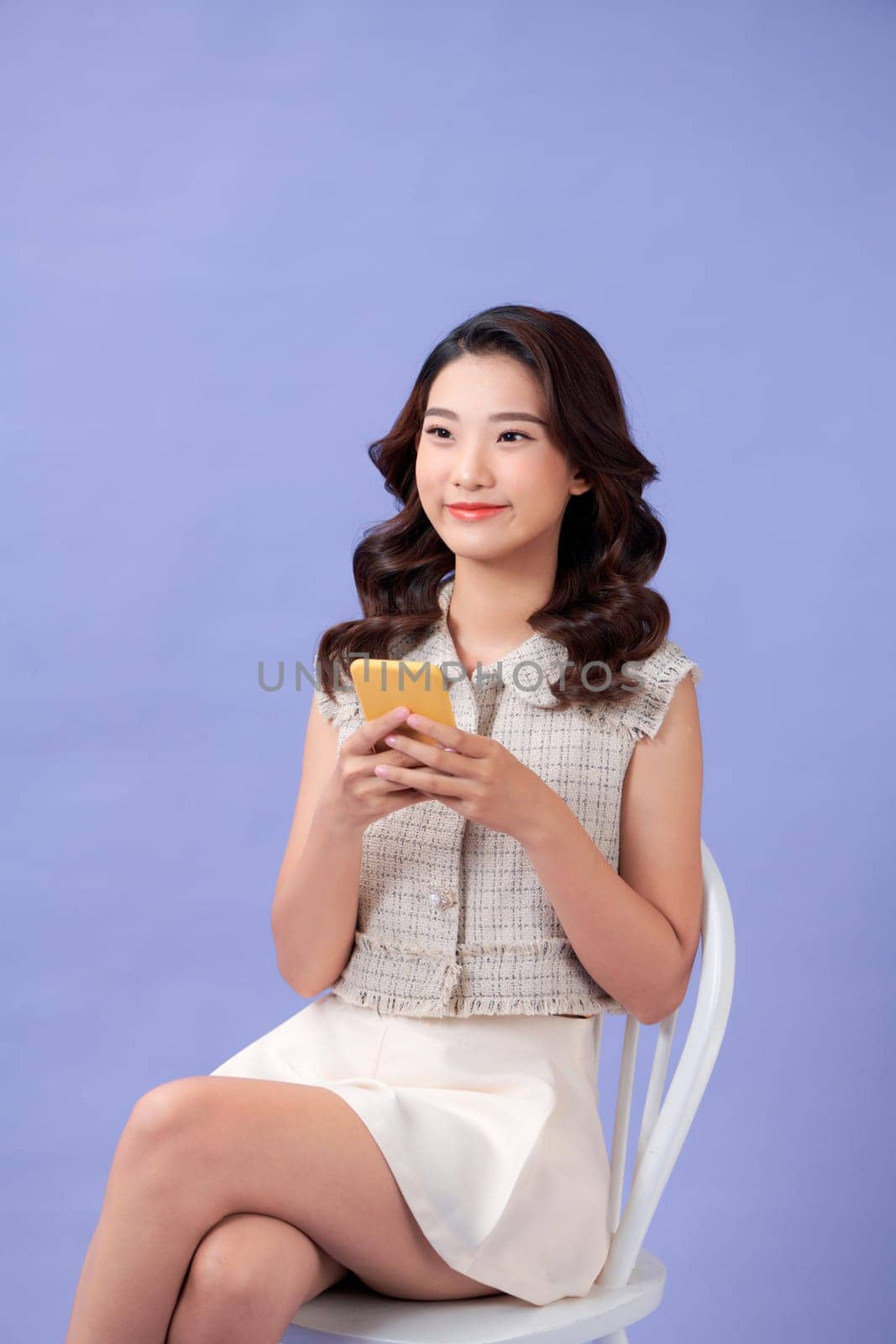 Young Asian woman sitting and using smartphone on purple background by makidotvn