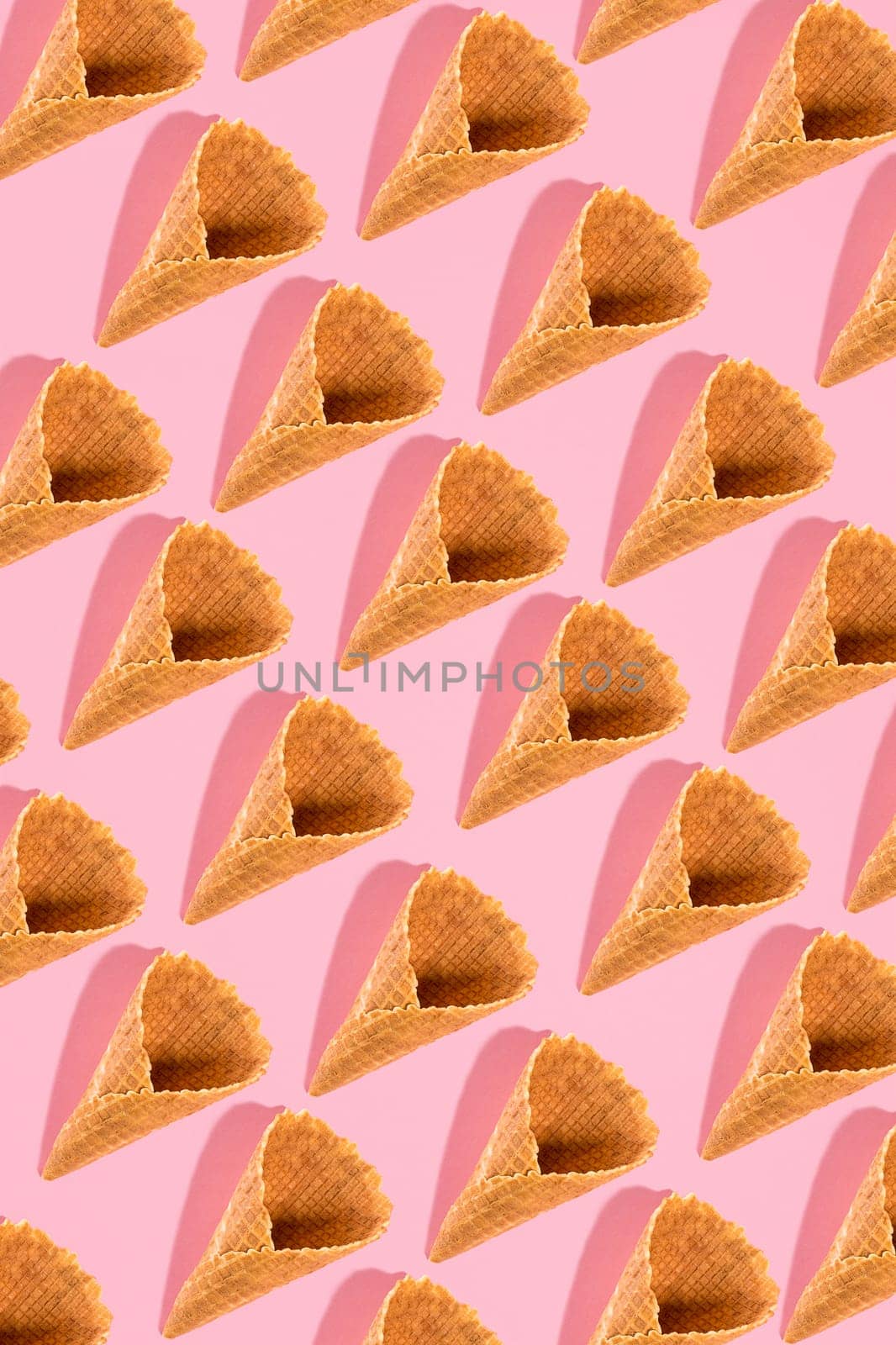 Sugar waffle cone for ice cream arranged in pattern on pink background. The image with copy space can be used as a background for the design of the confectionery menu, cards, greetings, invitations, pattern