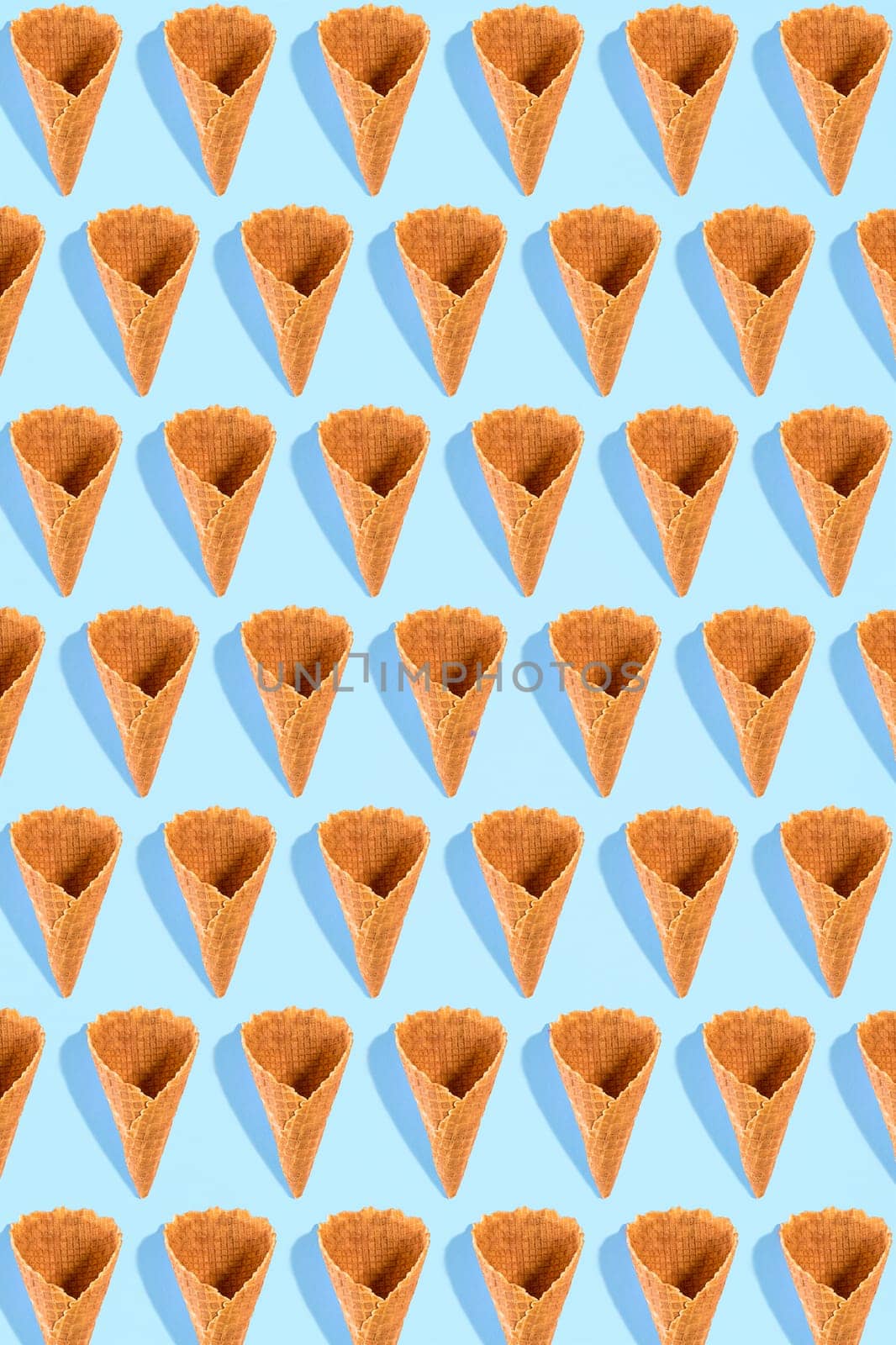 Sugar waffle cone for ice cream arranged in pattern on mint background. The image with copy space can be used as a background for the design of the confectionery menu, cards, greetings, invitations, pattern