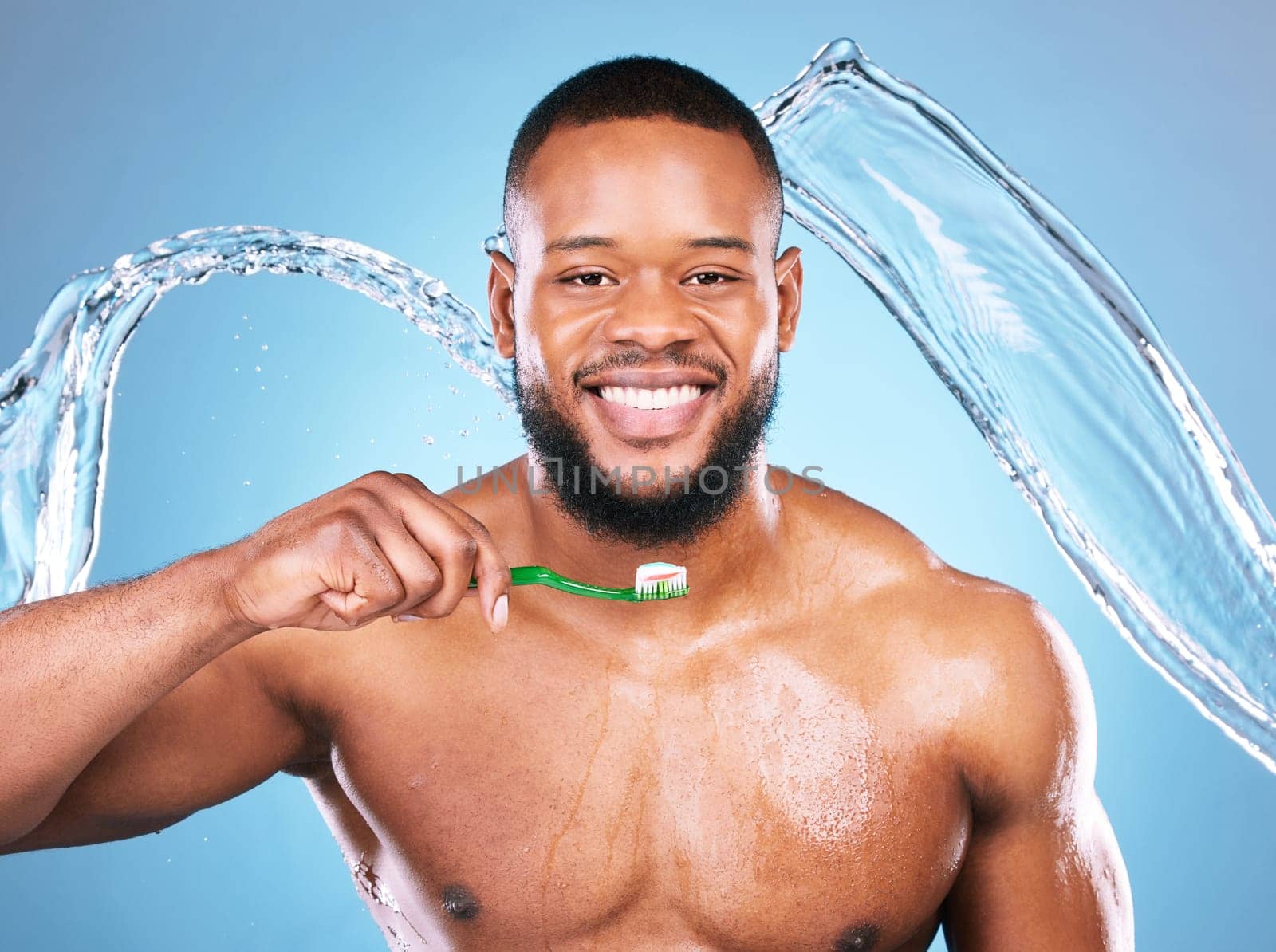 Black man, face and toothbrush with splash of water, dental and brushing teeth for hygiene on blue background. Cleaning, wet and male in portrait with smile for oral care product and toothpaste by YuriArcurs
