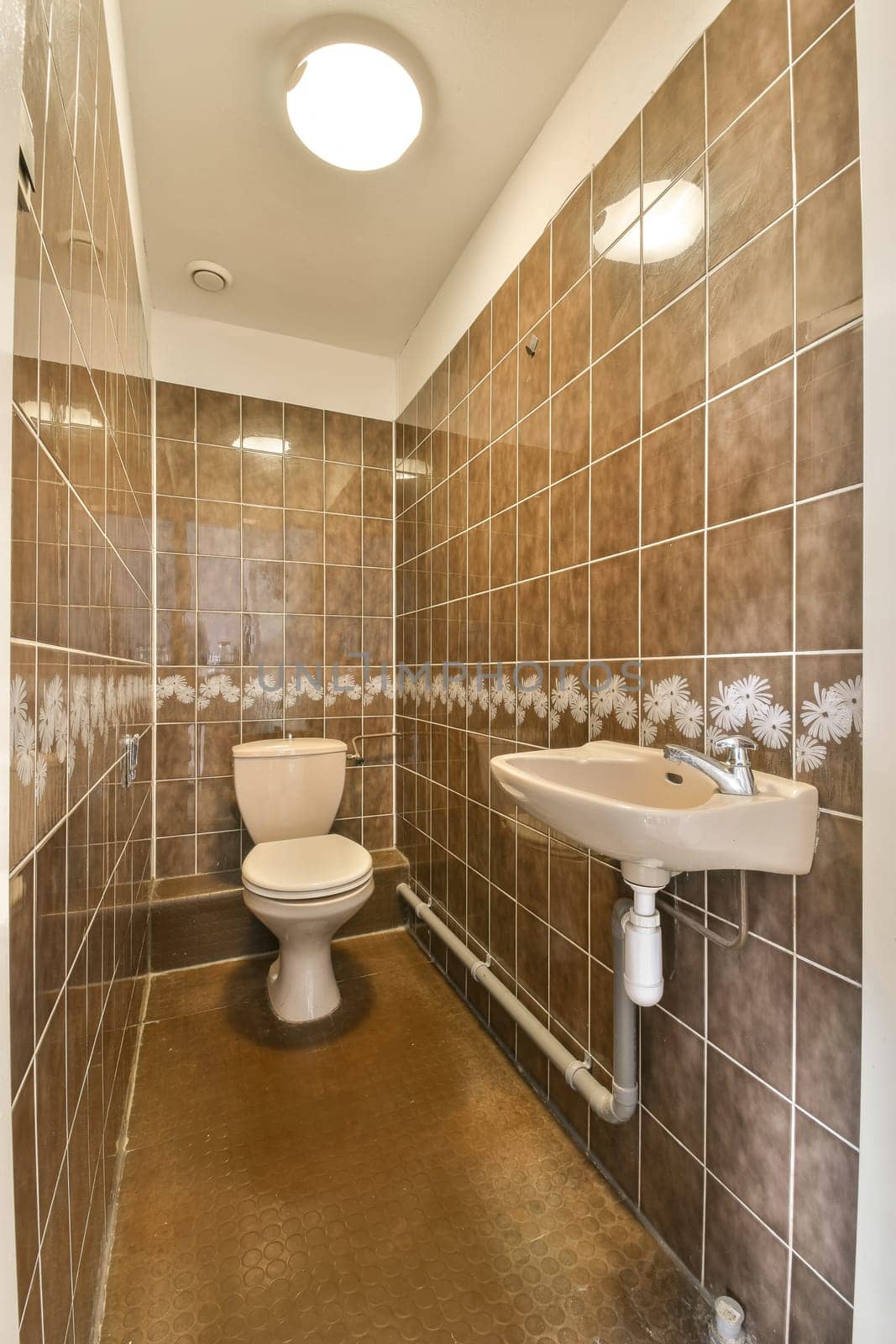 a bathroom with brown tiles on the walls and white fixtures in the sink is next to the toilet, which has been used for