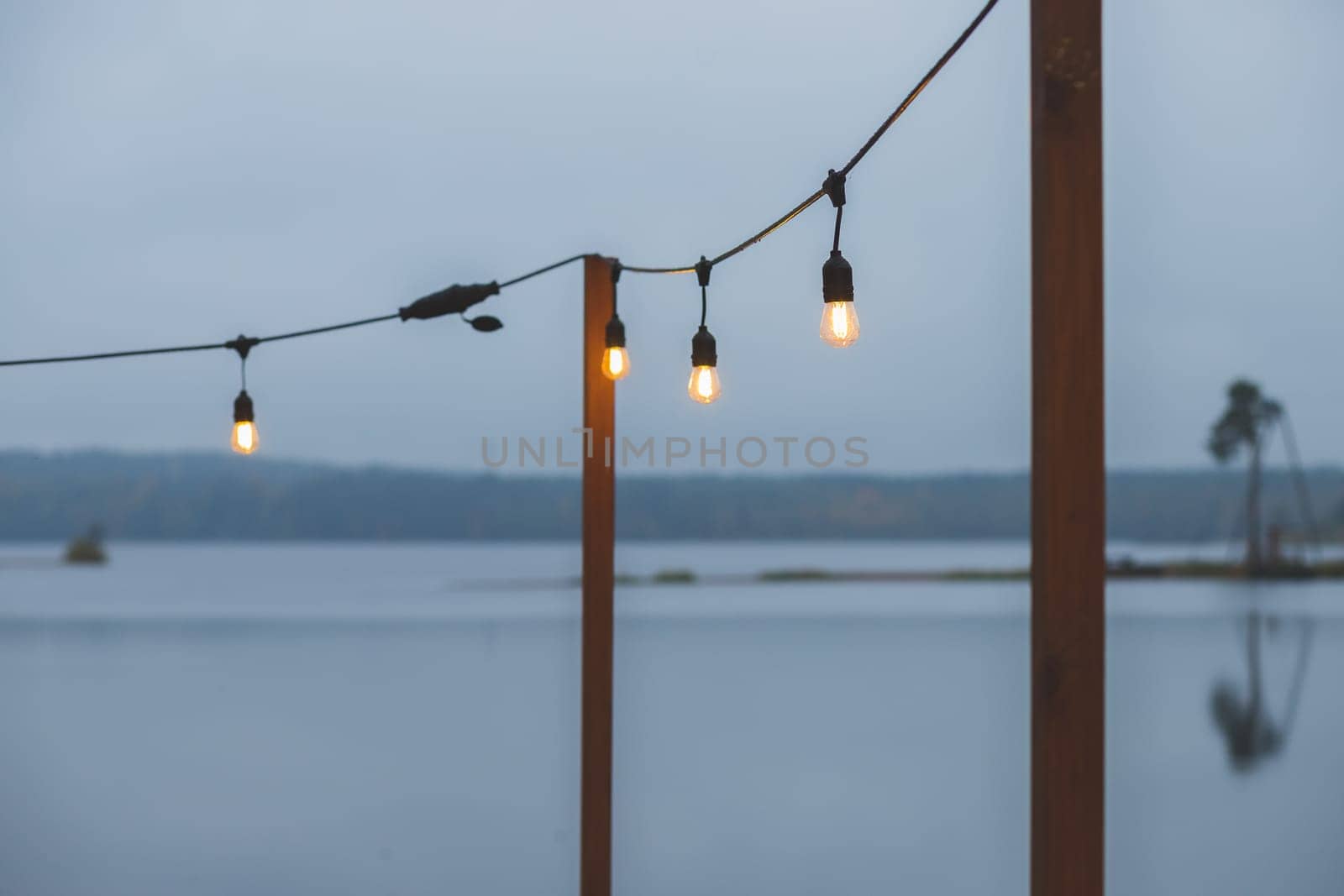 Twilight, gray color sky at the lakescape, electric lamps as garland and wooden terrace, pier.
