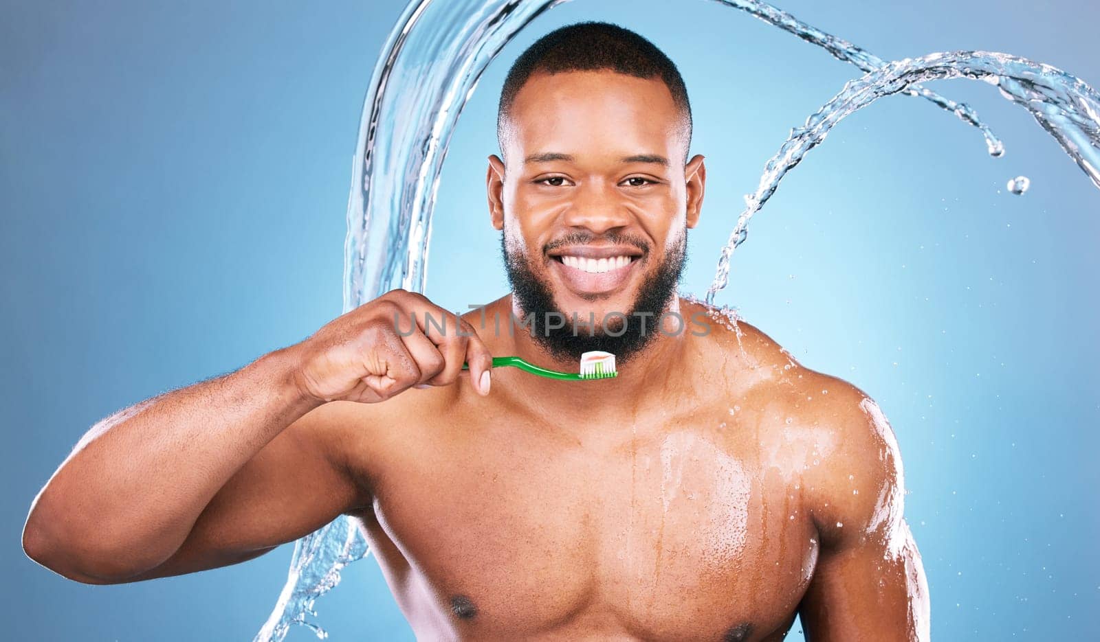 Black man, face and toothbrush with water splash and dental, brushing teeth and hygiene on blue background. Cleaning, wet and grooming, male in portrait and smile for oral care product and toothpaste by YuriArcurs