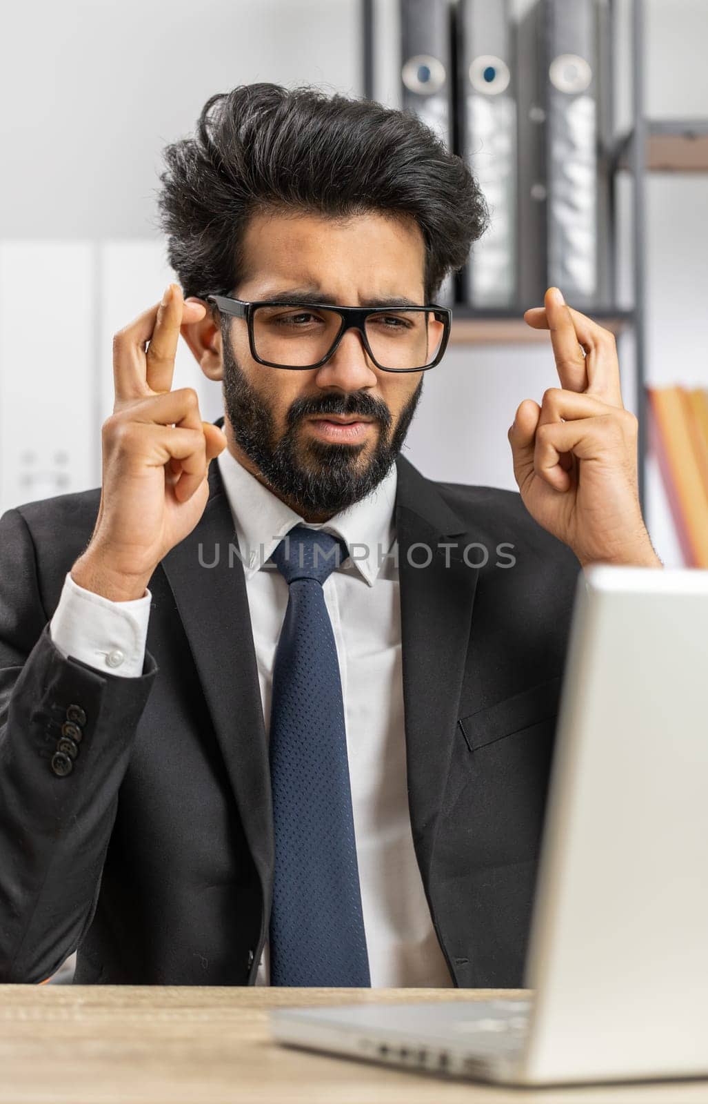 Bearded indian businessman crossed fingers looking at laptop screen asking for good luck news, wishing good exam results, dreaming about win victory in lottery jackpot, business money profit at office