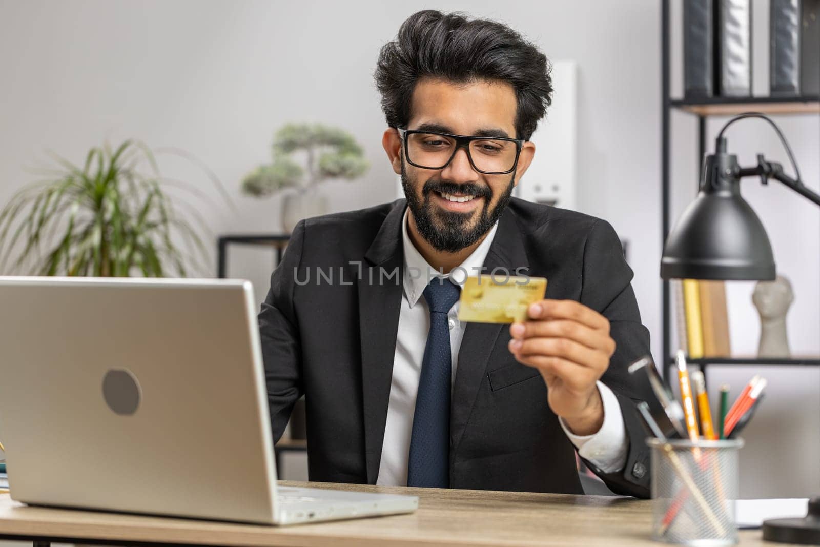 Bearded businessman programmer software developer working making online purchase payment shopping with credit bank card and use laptop at home office desk with laptop. Indian freelancer business man