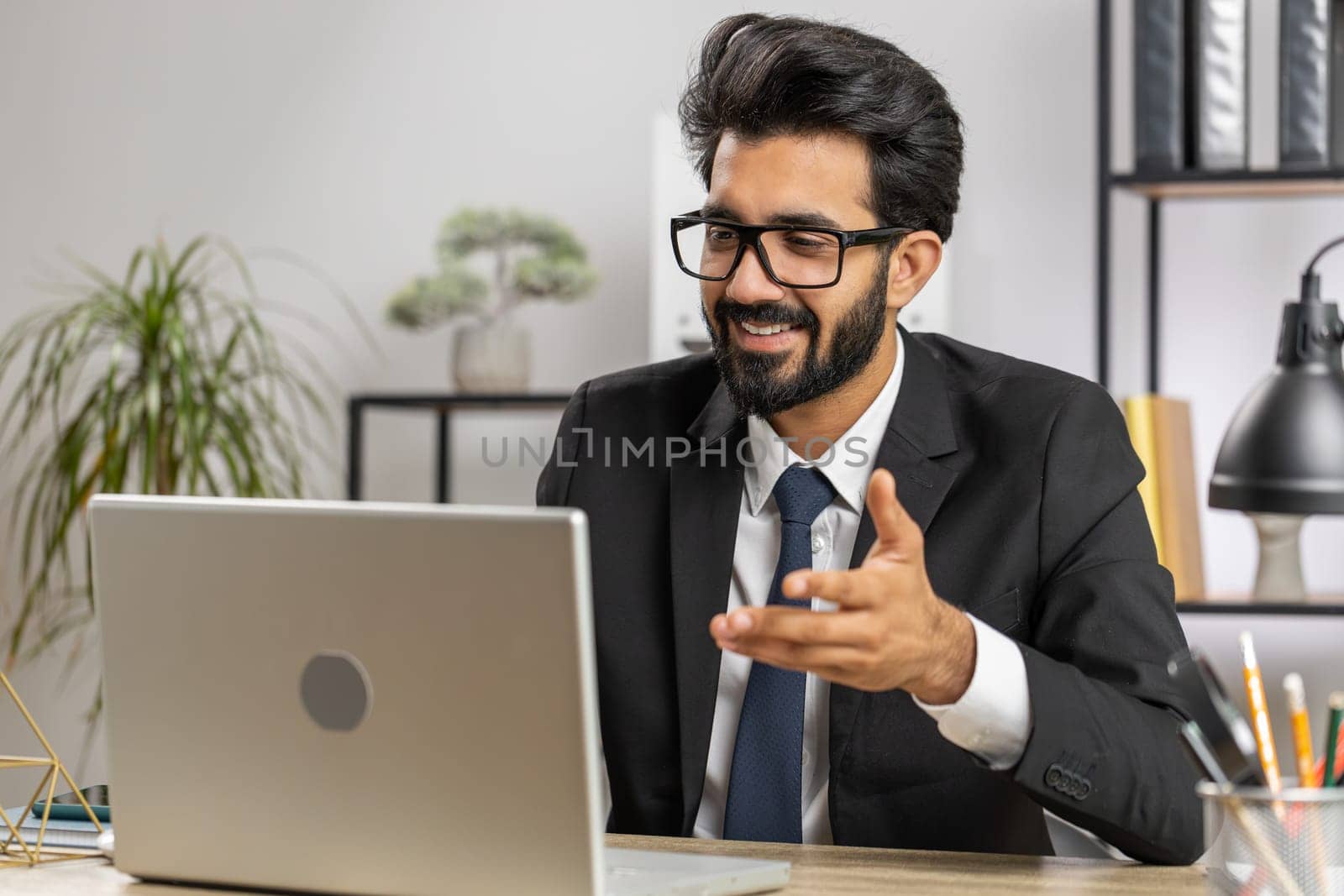 Indian businessman working on laptop computer at home office desk talk on online communication video call with employee, boss. Manager man freelancer support services looking at webcam of computer