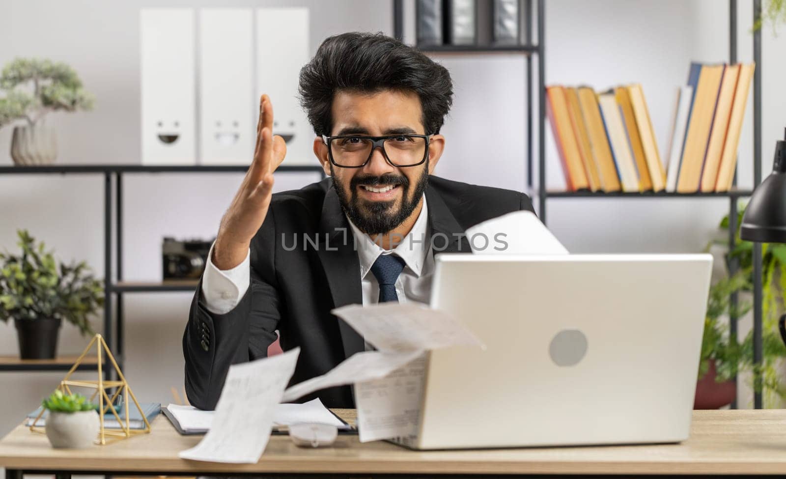 Stressed indian businessman working looking at unpaid bank debt bills, doing paperwork, planning budget, calculate finances mortgage payments at office. Displeased freelancer man throws paper bills