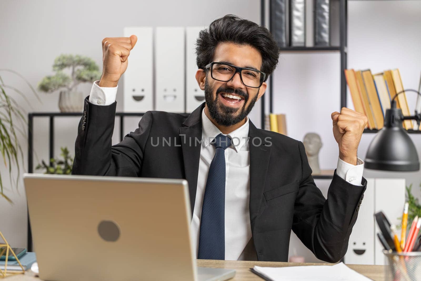 Happy amazed young indian businessman working on laptop shocked by sudden victory, game winning, lottery goal achievemen, good career news. Excited manager man freelancer at home office workplace desk