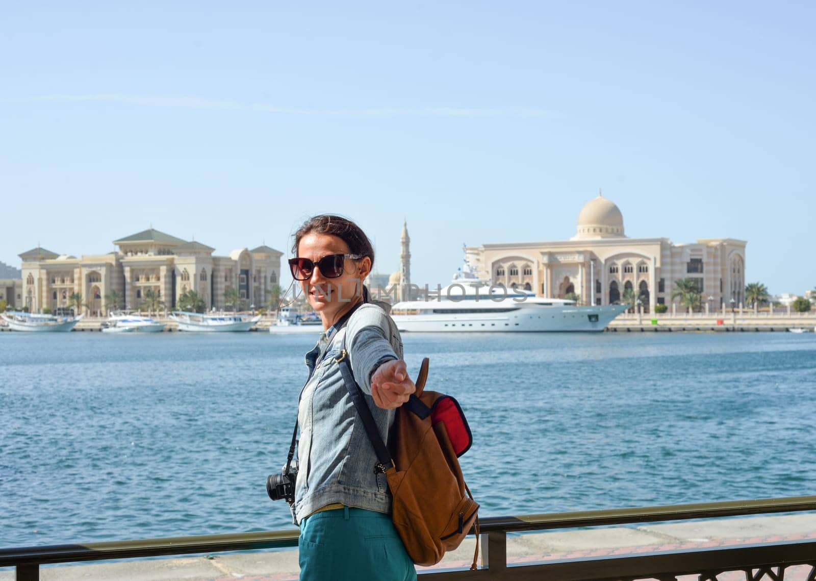 A young woman tourist with a backpack looks at the administrative region of the emirate of Sharjah with the port and ships