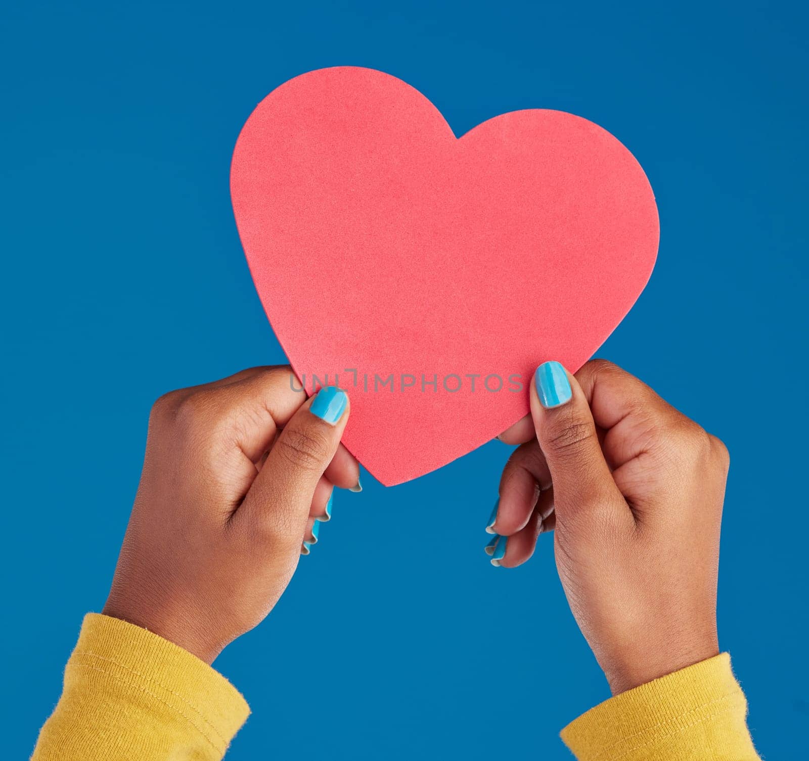 Paper, heart and hands of black woman in studio for love, date and kindness. Invitation, romance and feelings with female and shape isolated on blue background for emotion, support and affectionate.