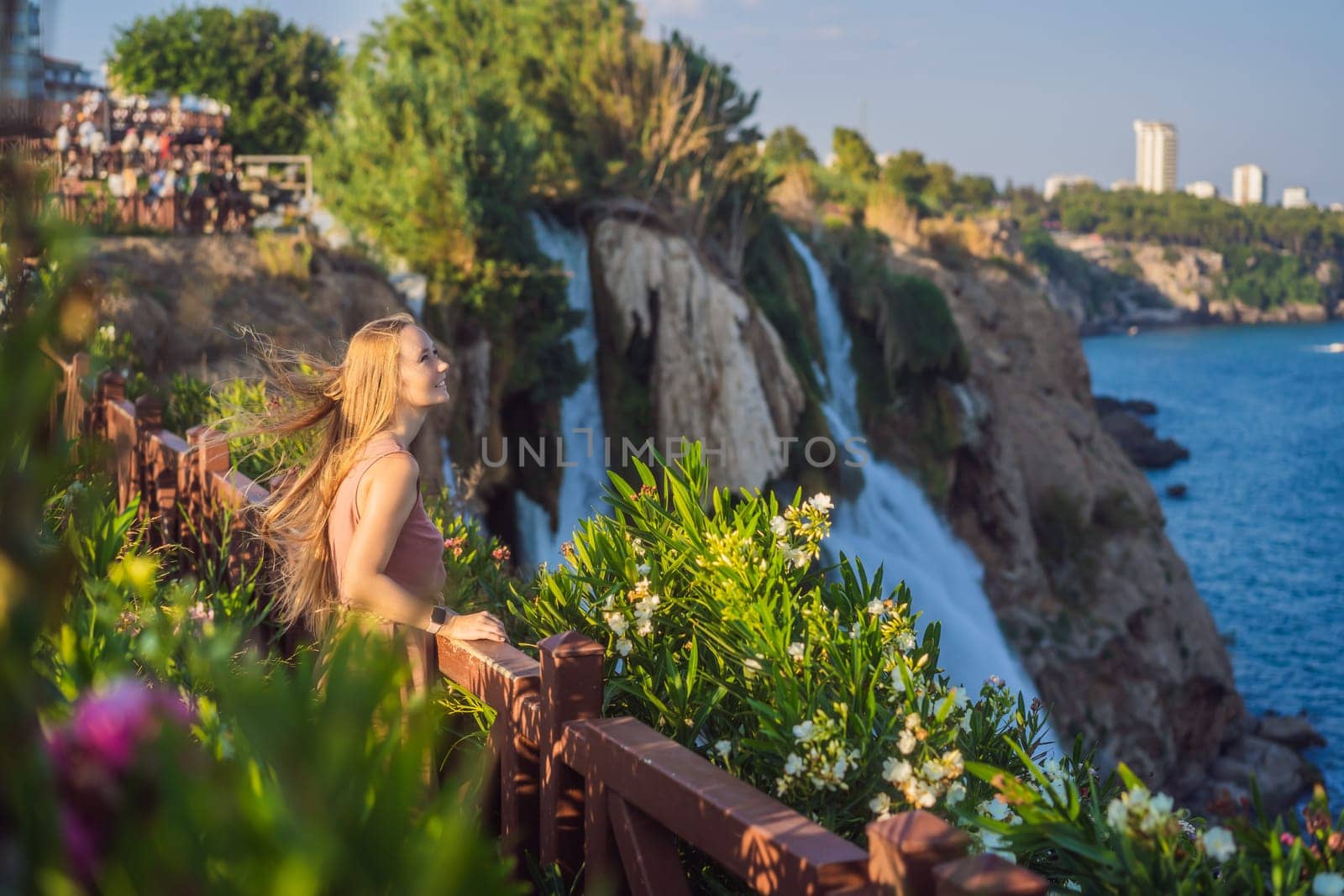 Beautiful woman with long hair on the background of Duden waterfall in Antalya. Famous places of Turkey. Lower Duden Falls drop off a rocky cliff falling from about 40 m into the Mediterranean Sea in amazing water clouds. Tourism and travel destination photo in Antalya, Turkey. Turkiye.